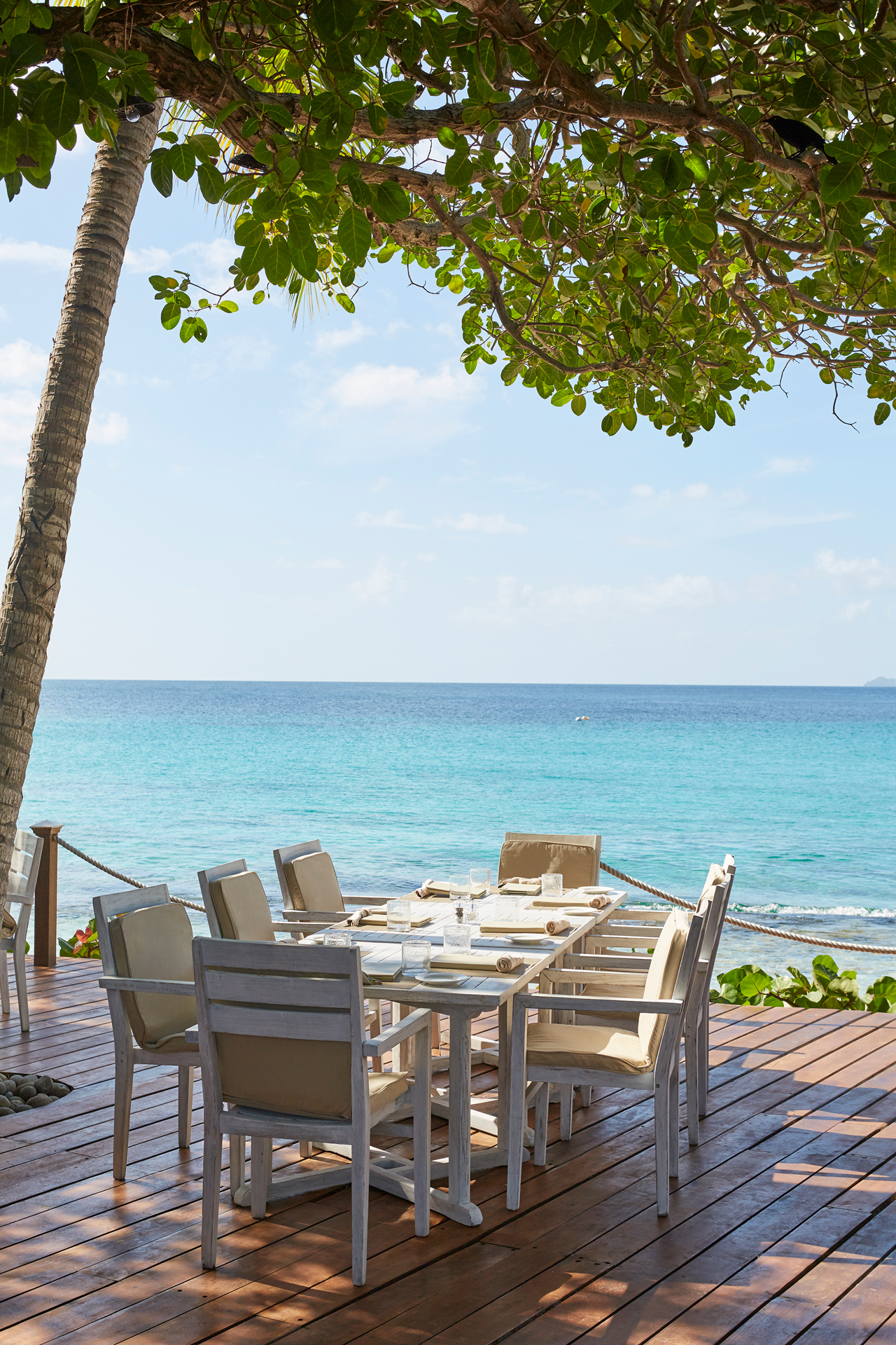 A long dining table on a wooden deck next to the sea