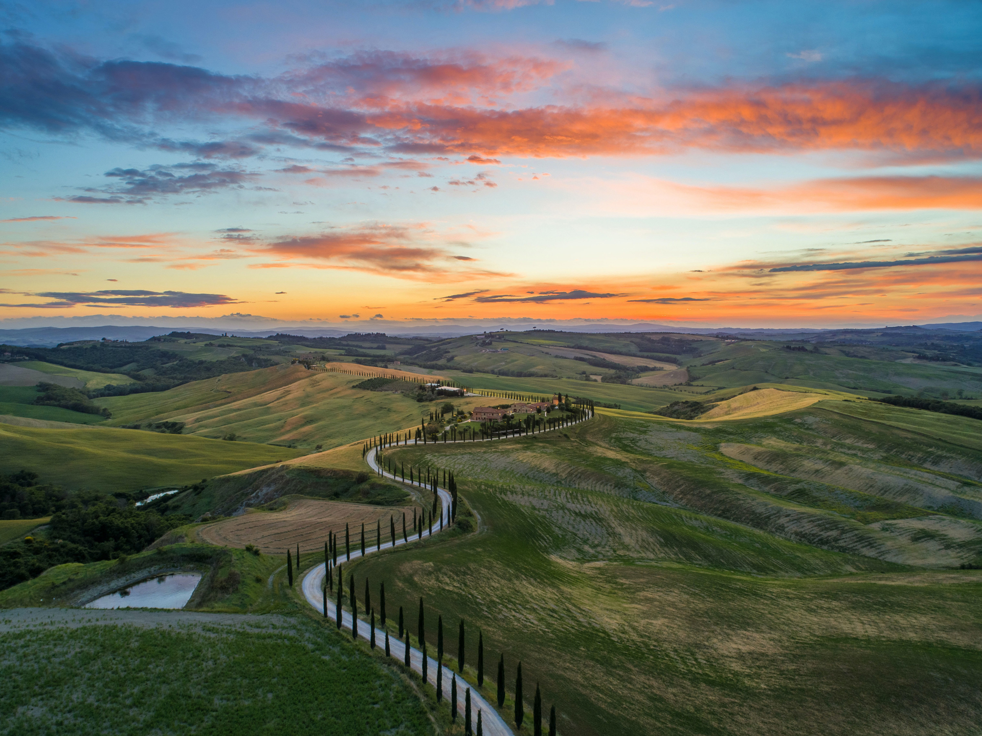 A road running between green grass fields on rolling hills as the sun sets