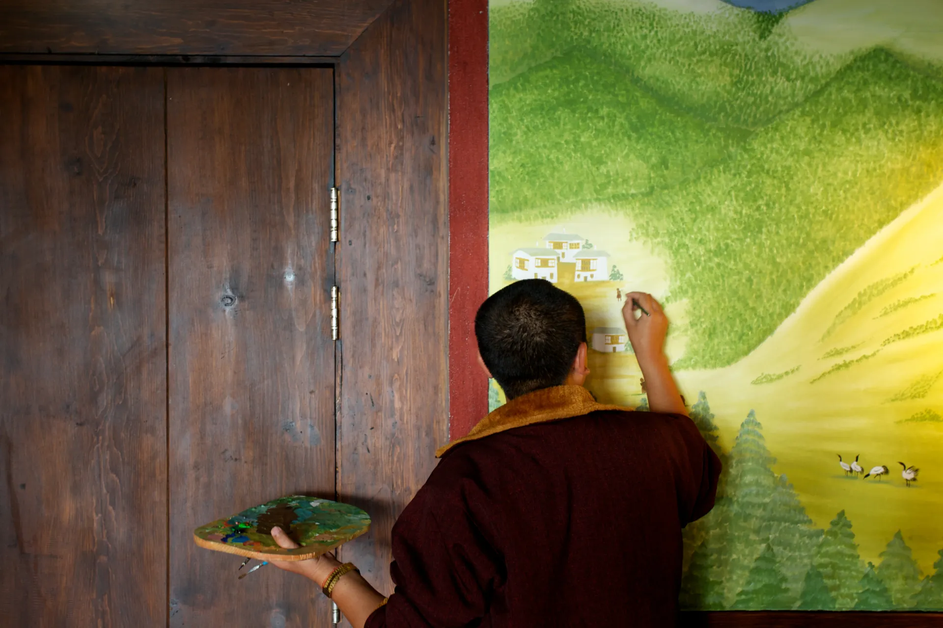 Person painting a detailed mural of a landscape on an interior wall.