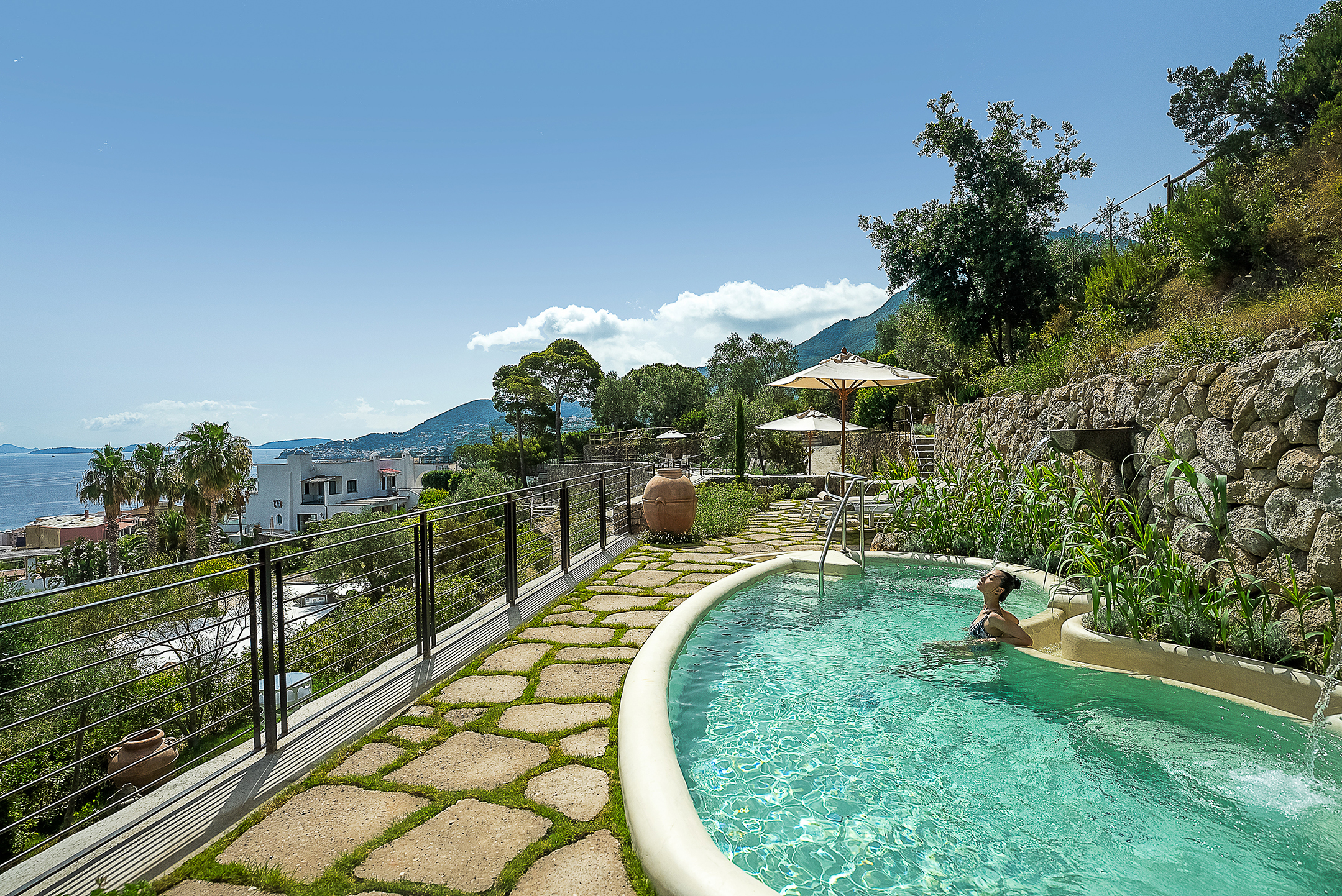 Relaxing hotspring view at Botania Relais & Spa in Ischia with a person relaxing in pool scenic ocean and mountain backdrop.