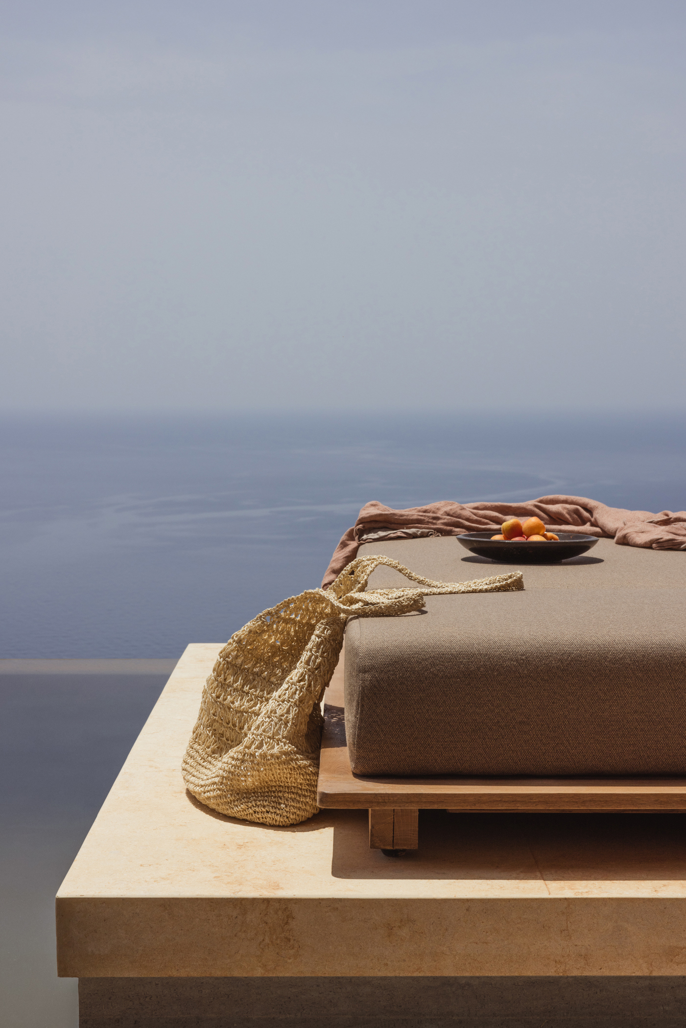 The corner of a sun lounger beside a pool at Gundari with a woven beach bag and bowl of fruit