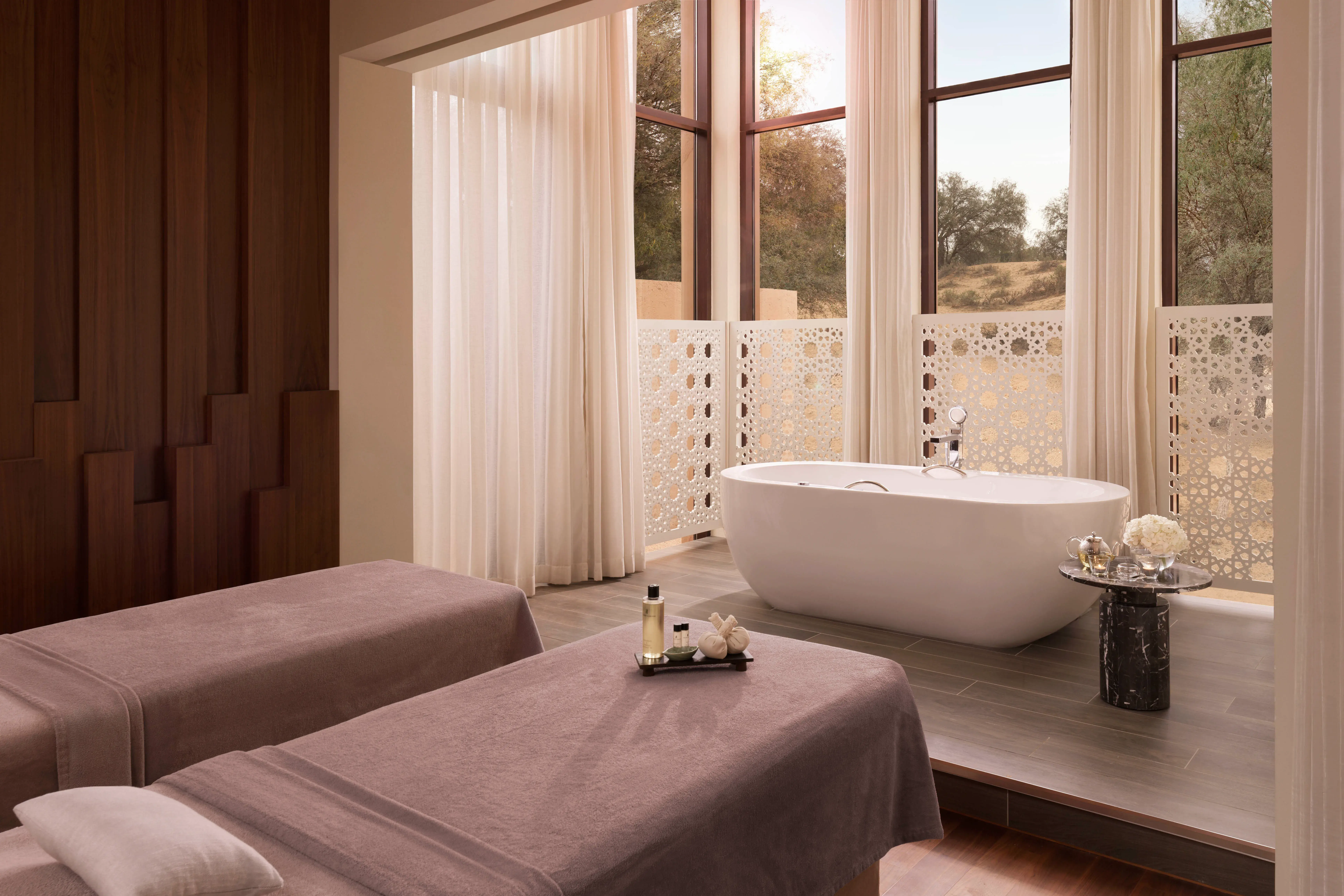 Luxury spa treatment room at Ritz-Carlton Ras Al Khaimah, Al Wadi Desert featuring two massage tables and a freestanding bathtub with desert views.