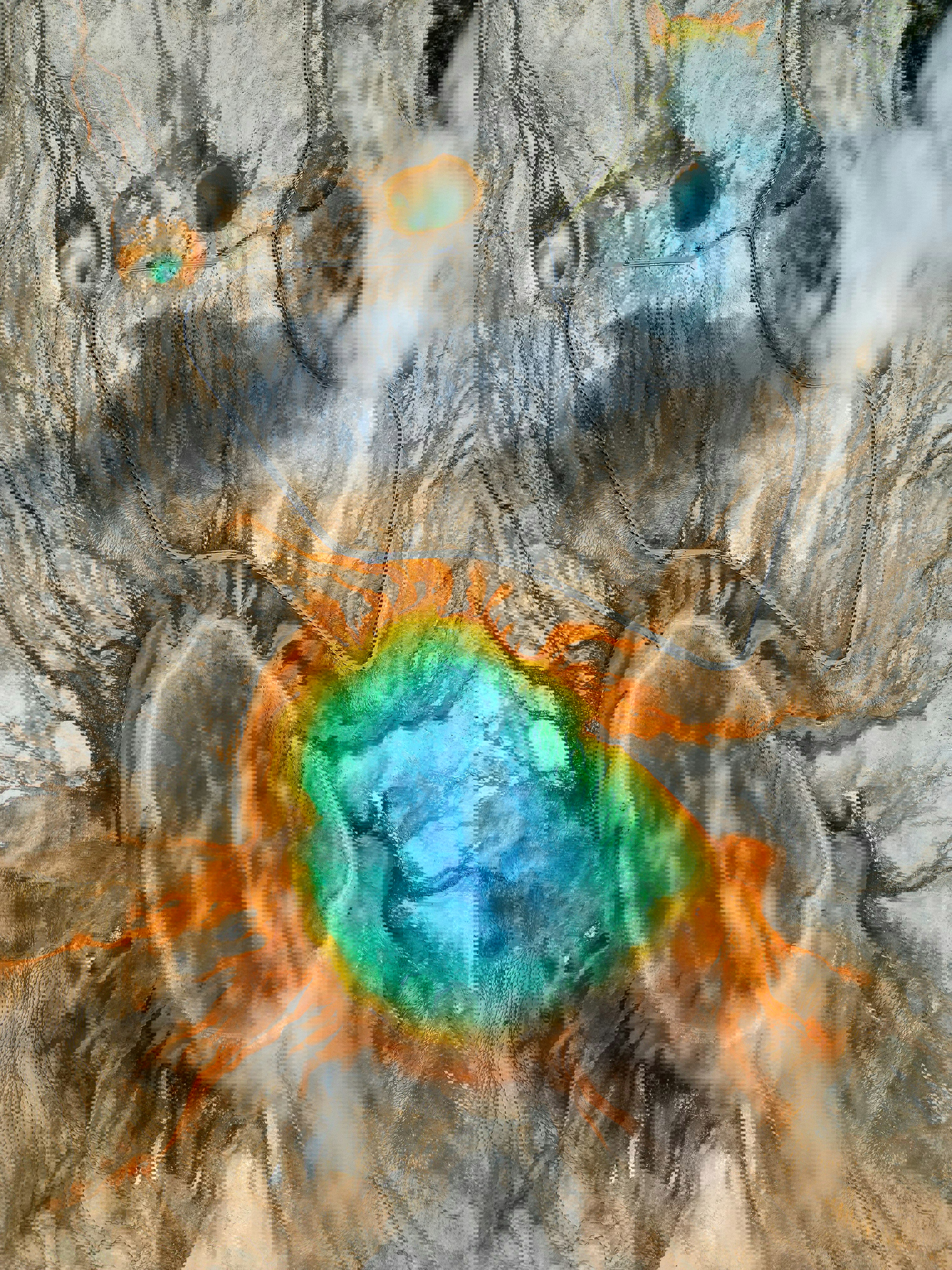 A bird's-eye view of a geyser in Yellowstone National Park where a blue pool is surrounded by red and yellow earth