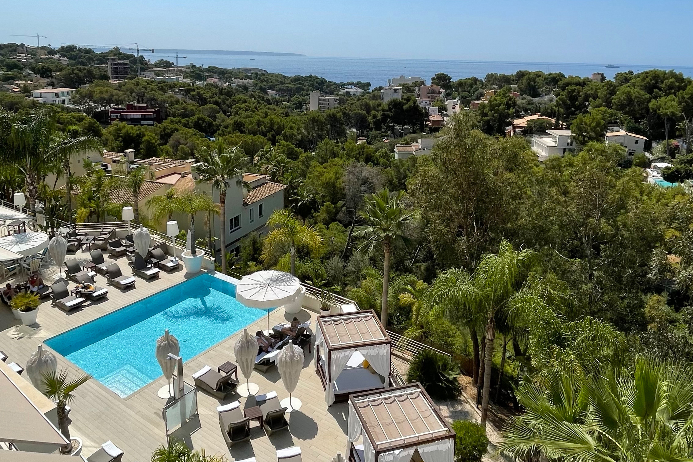 Luxurious outdoor pool area at Portals Hills in Mallorca with lounge chairs, cabanas, lush greenery, and sea views.