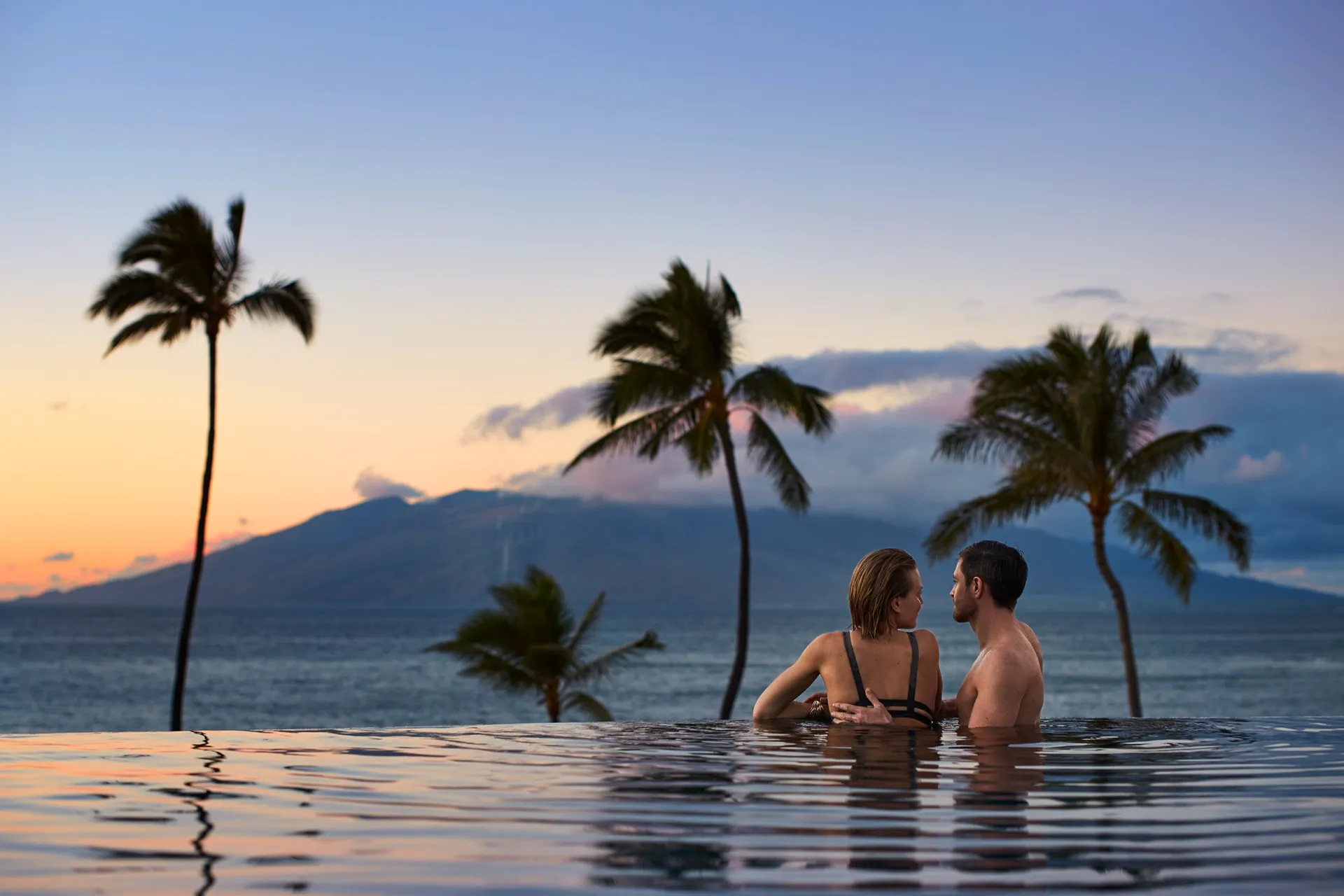 Couple in a pool with palm trees and mountains at sunset