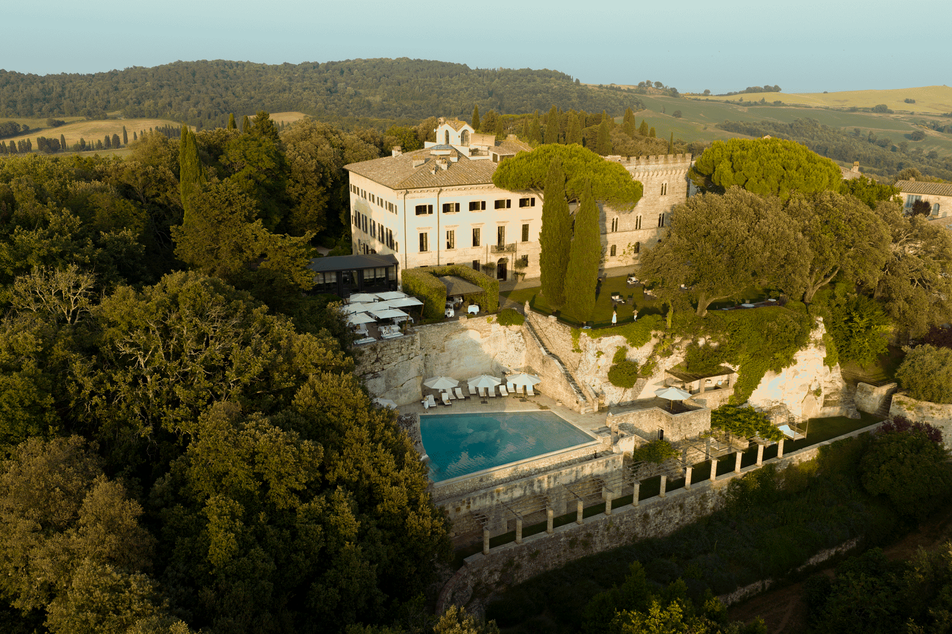 Aerial view of a historic countryside estate surrounded by trees, terraces, and a pool set within rolling hills.