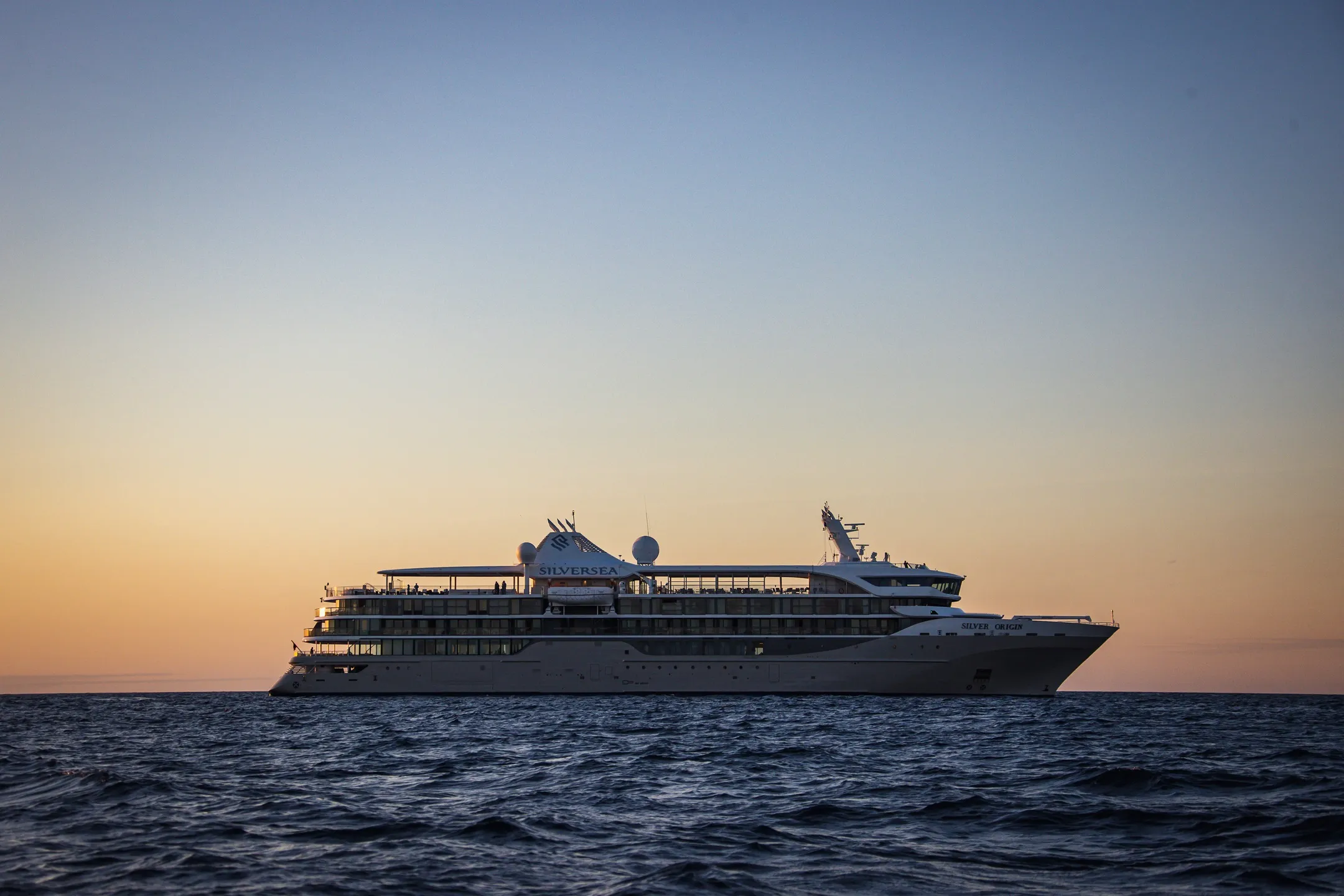Silversea cruise ship sailing on calm ocean waters at sunset under a clear sky.