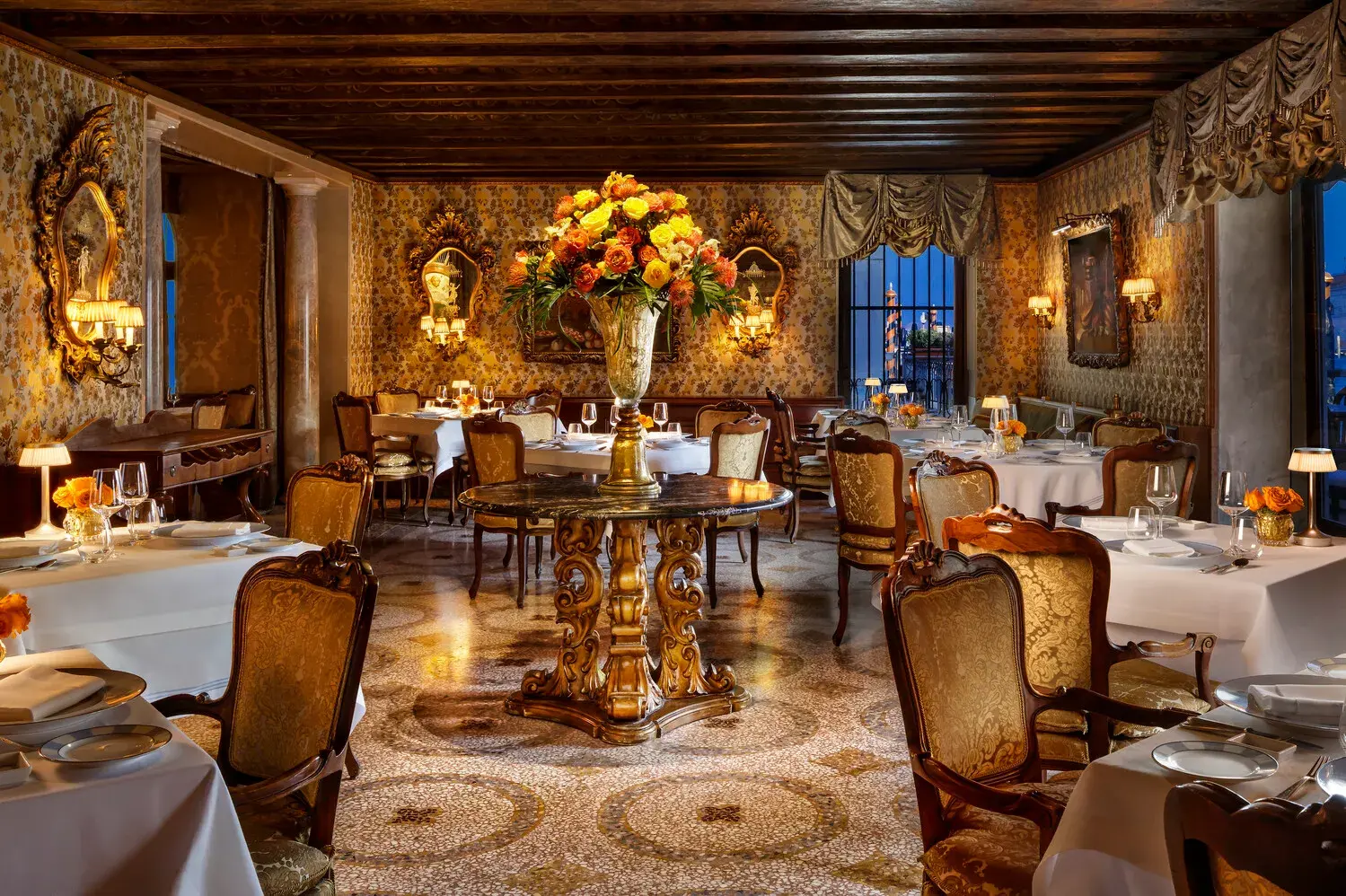 Elegant fine dining restaurant at The Gritti Palace in Venice featuring ornate décor, golden tones, and a central floral arrangement.