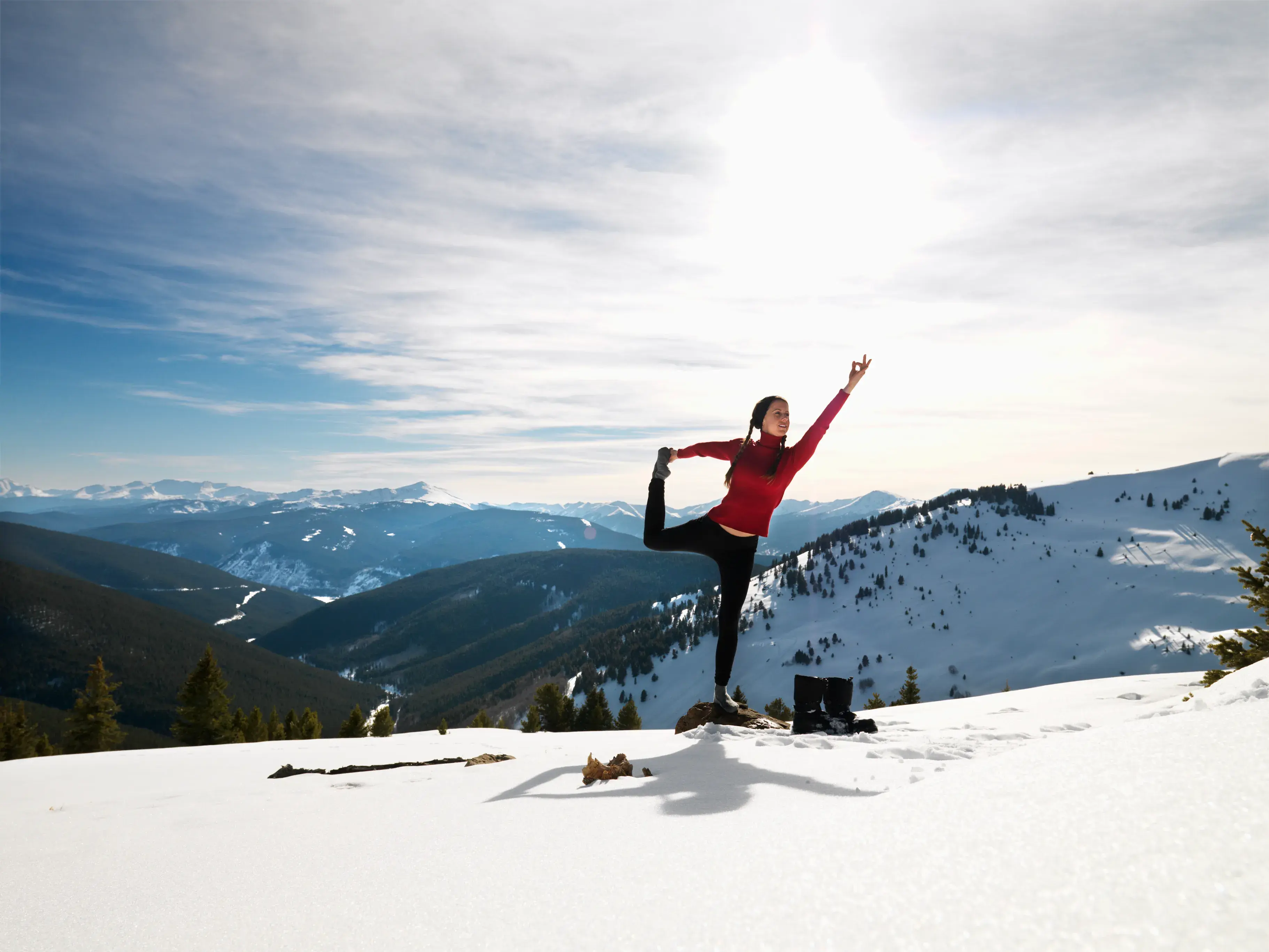 A woman practicing yoga on the top of a snowy mountain under a clear sky