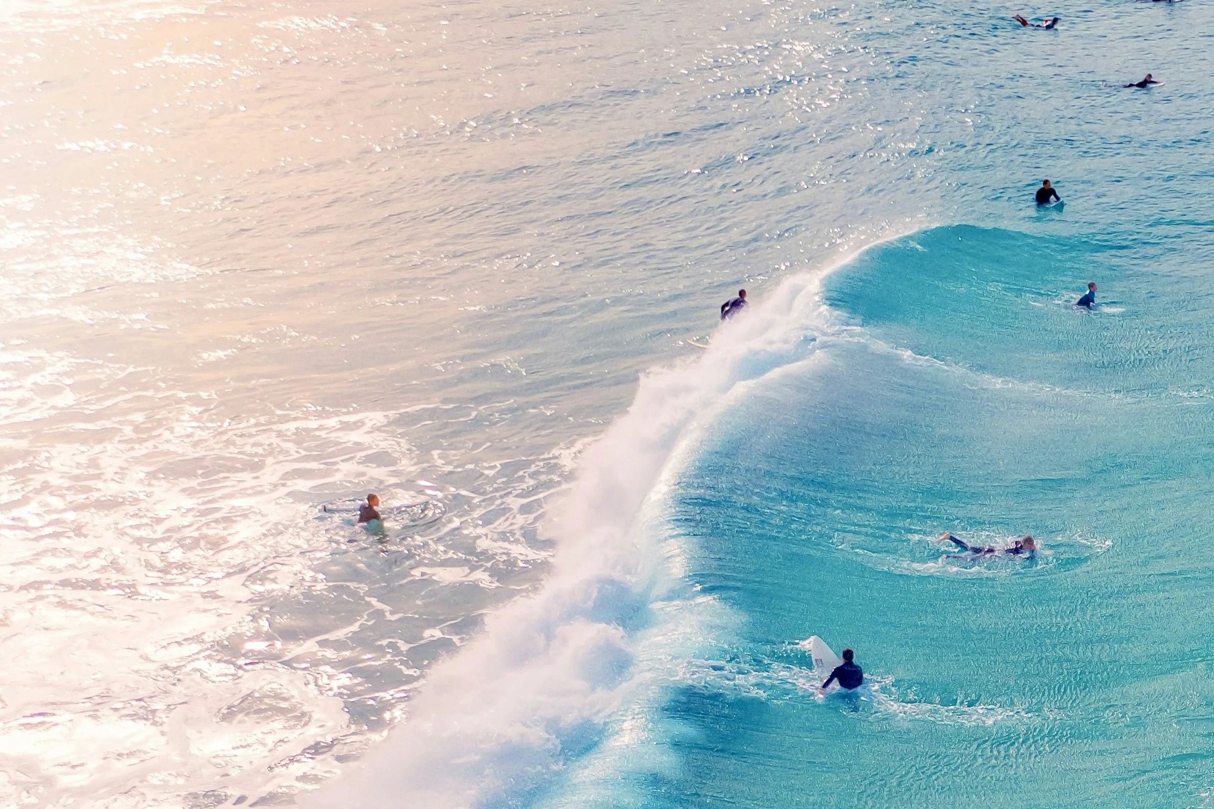 A group of surfers riding and waiting for waves in the ocean during sunset.