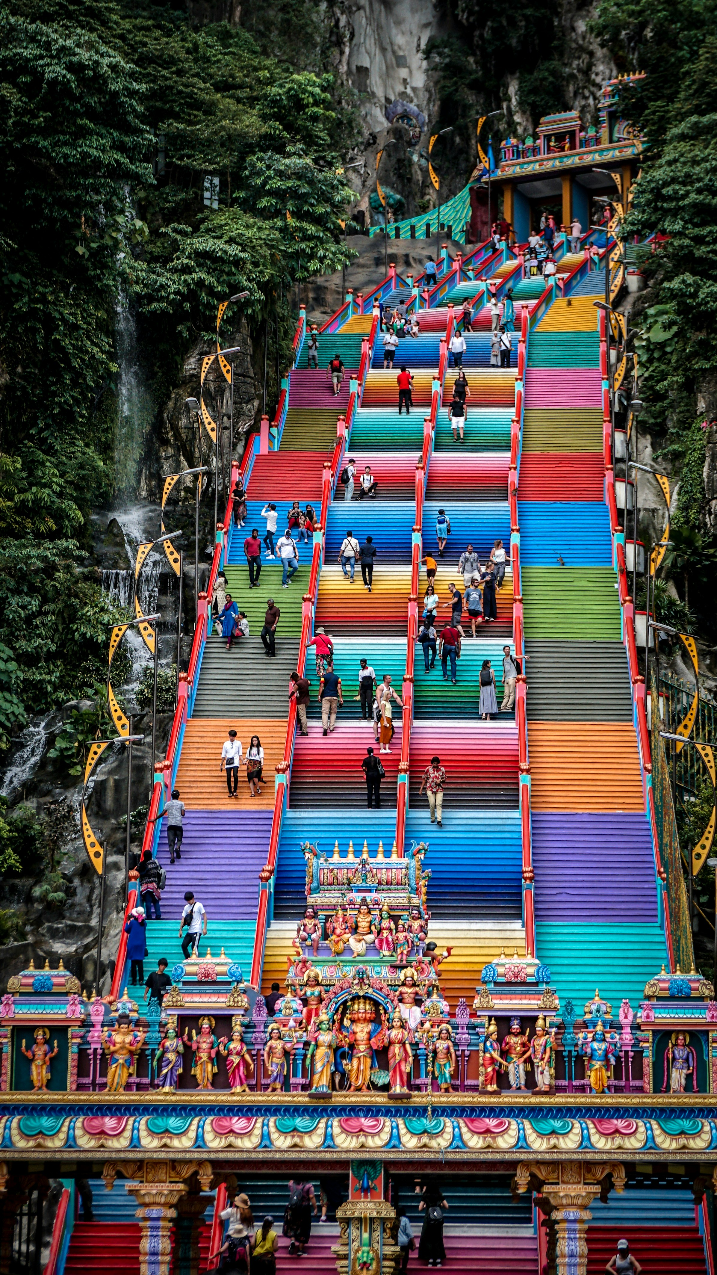 People walking up and down the 272 colourful steps leading to the temple at Batu Cave with Hindu sculptures at the entrance