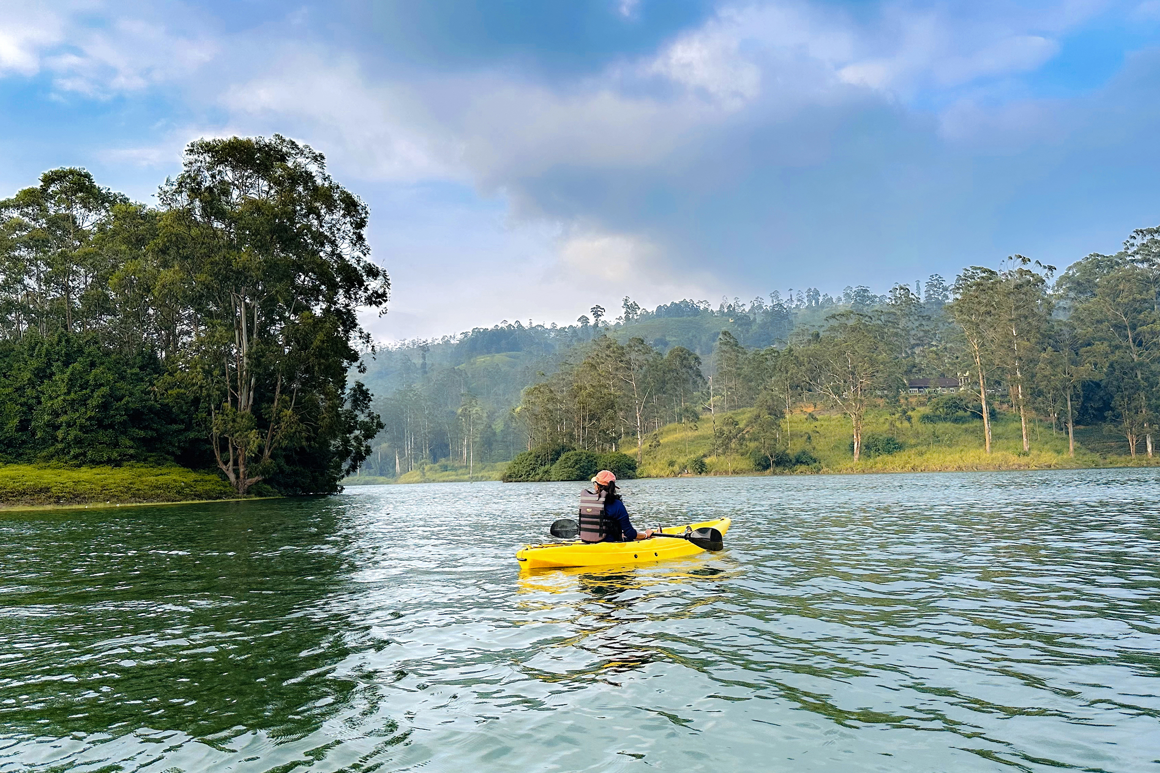 A person in a yellow kayak on the calm surface of Castlereagh Reservoir with trees in the background
