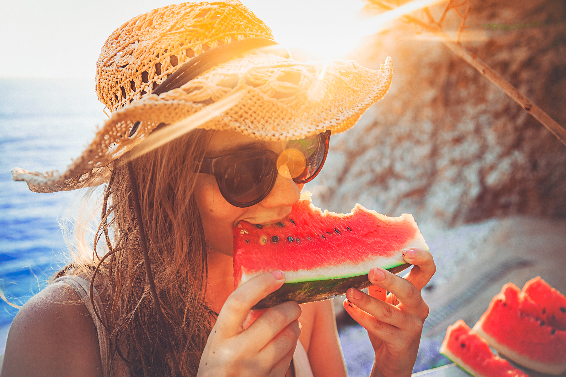 A girl wearing sunglasses and a straw hat eating a watermelon