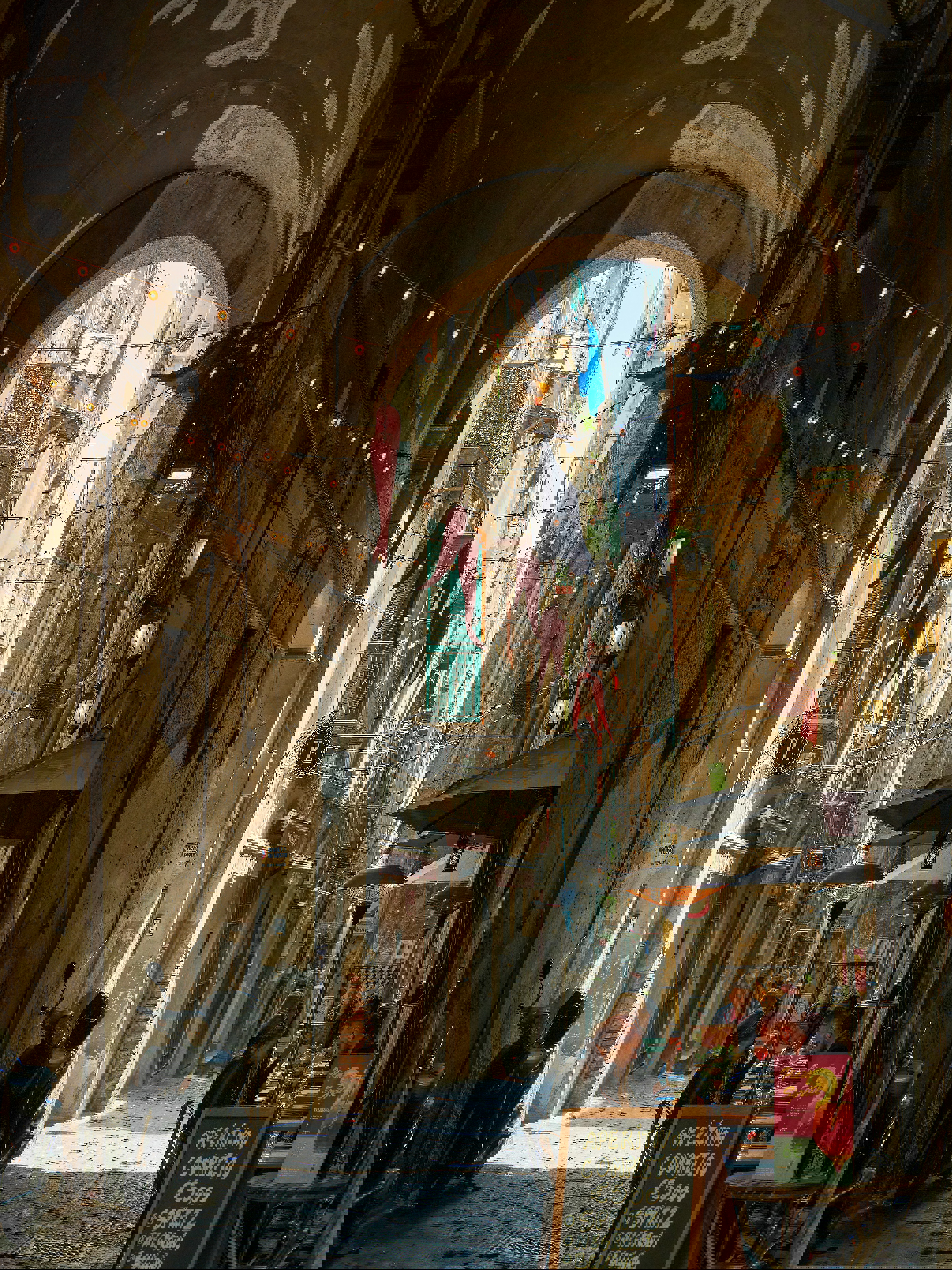 Charming narrow street in Naples with outdoor café seating under an archway and hanging decorations.