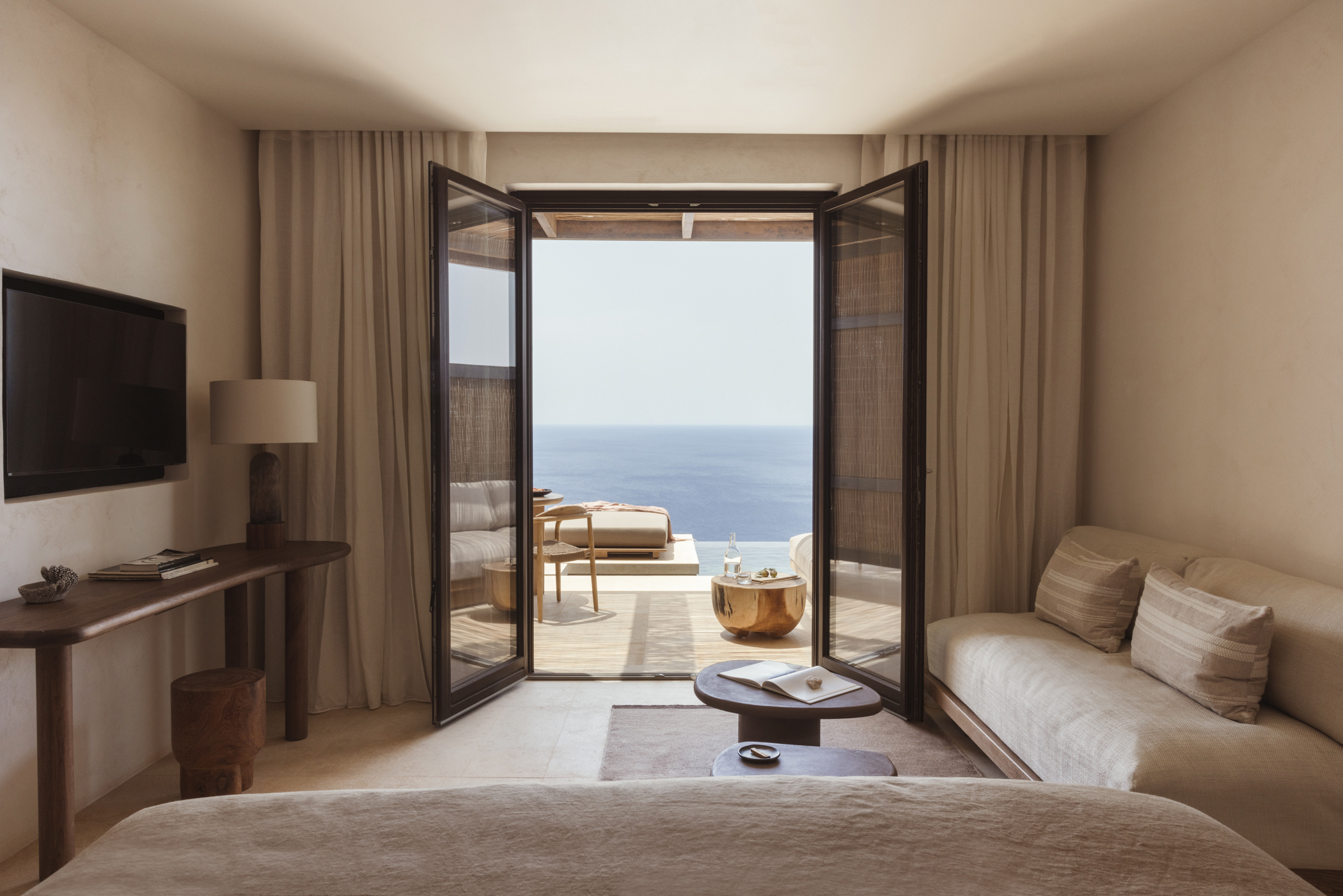 The view from an Executive Cave Suite lounge featuring plush sofas and an entertainment area, with large doors opening out onto a terrace featuring a table and pool with a sun lounger