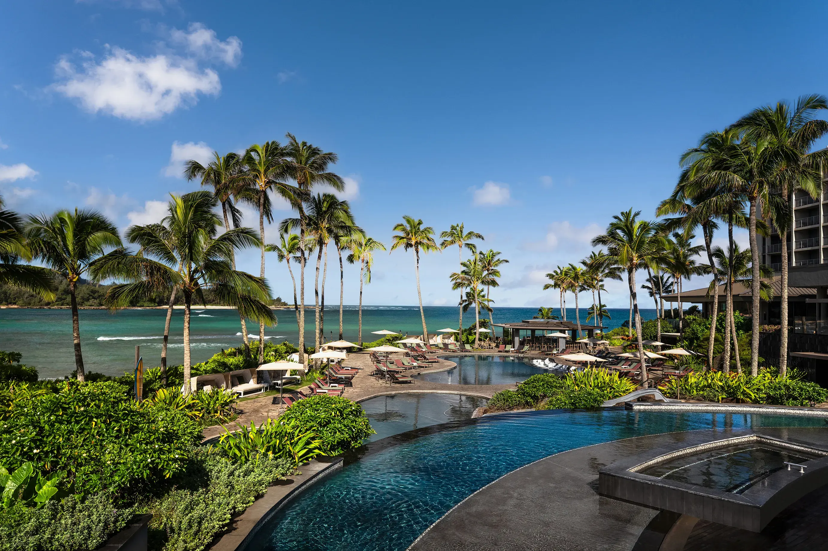 The main pool deck of Ritz-Carlton Turtle Bay featuring three swimming pools surrounded by palms and sun loungers with the ocean behind