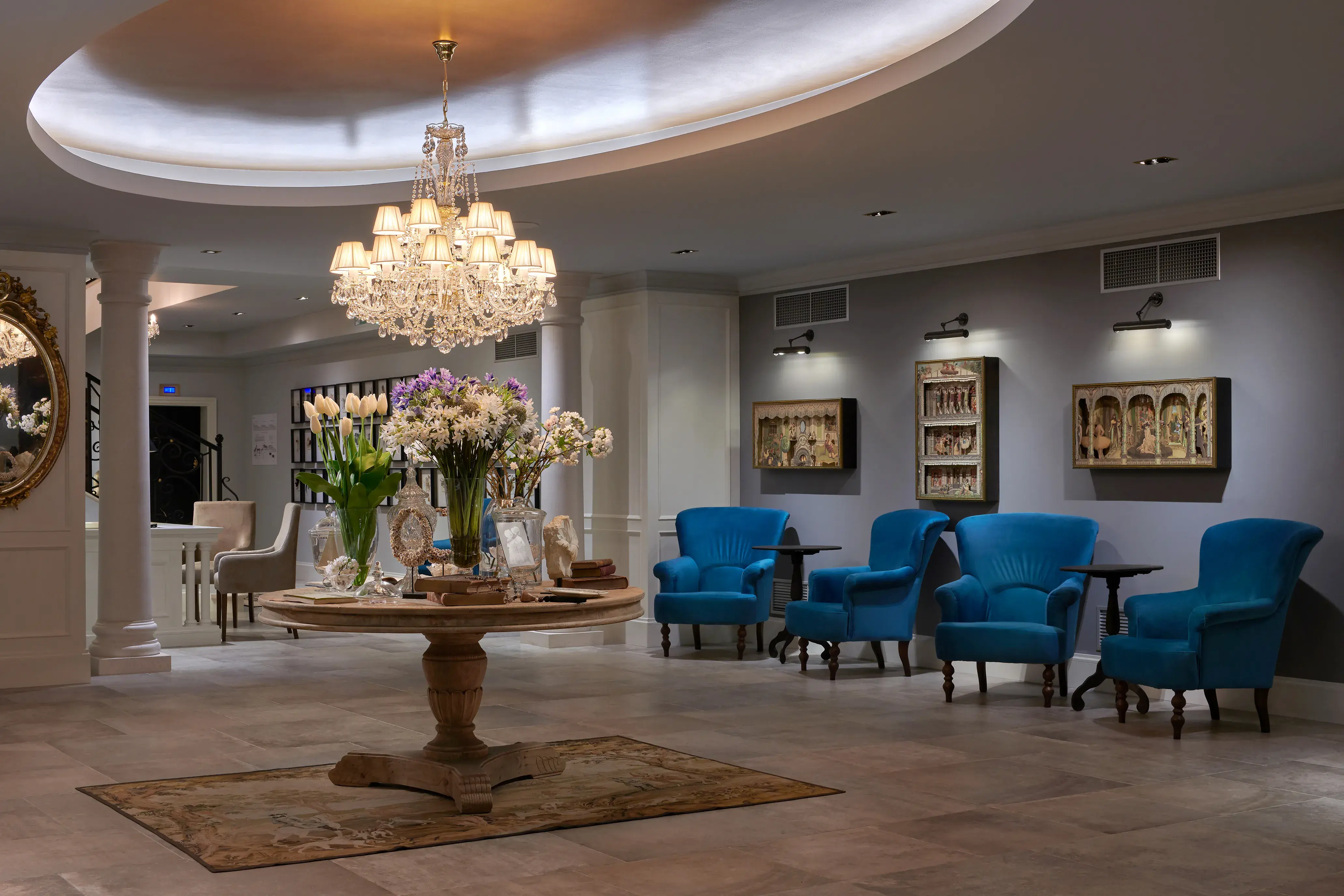 Lobby of Palace Elisabeth in Croatia featuring a large chandelier above a table decorated with flowers, with blue chairs behind and artifacts on the walls