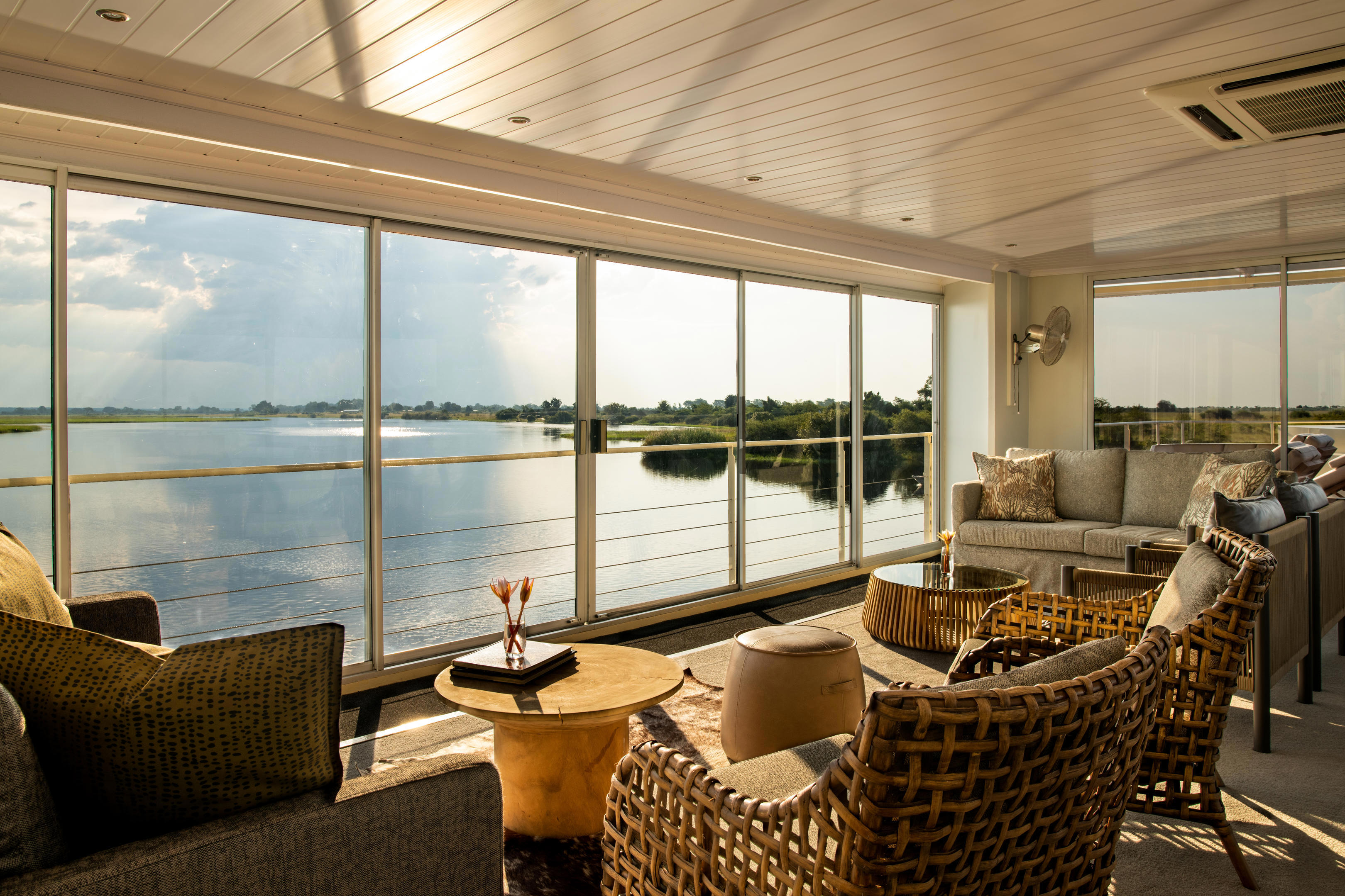 Plush lounge of Zambezi Queen with seating looking out over the river at sunset