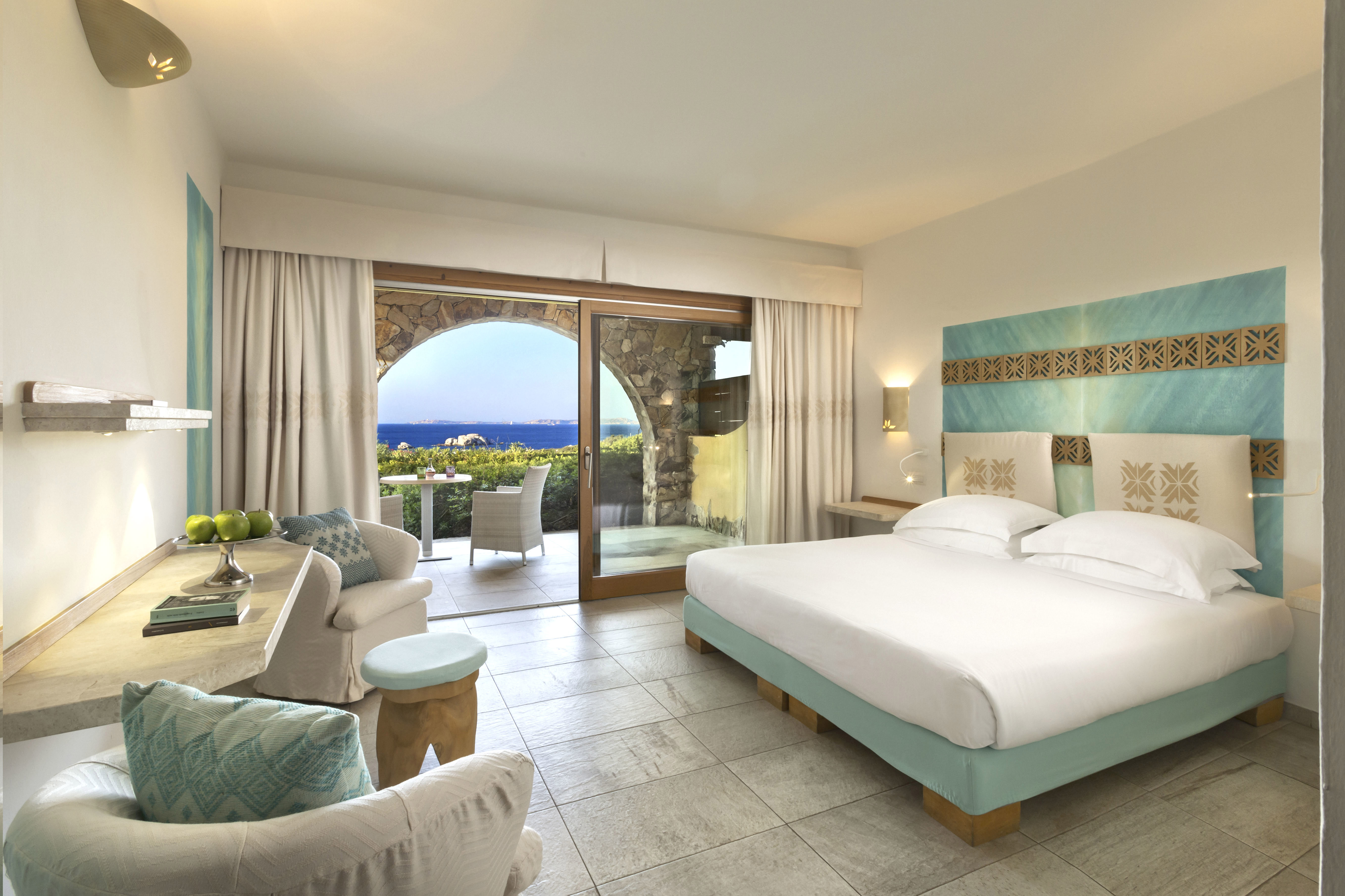 The large bedroom of a Superior Suite at La Licciola Hotel with comfy bed and marble desk area, featuring patio doors out to a seating area overlooking the sea