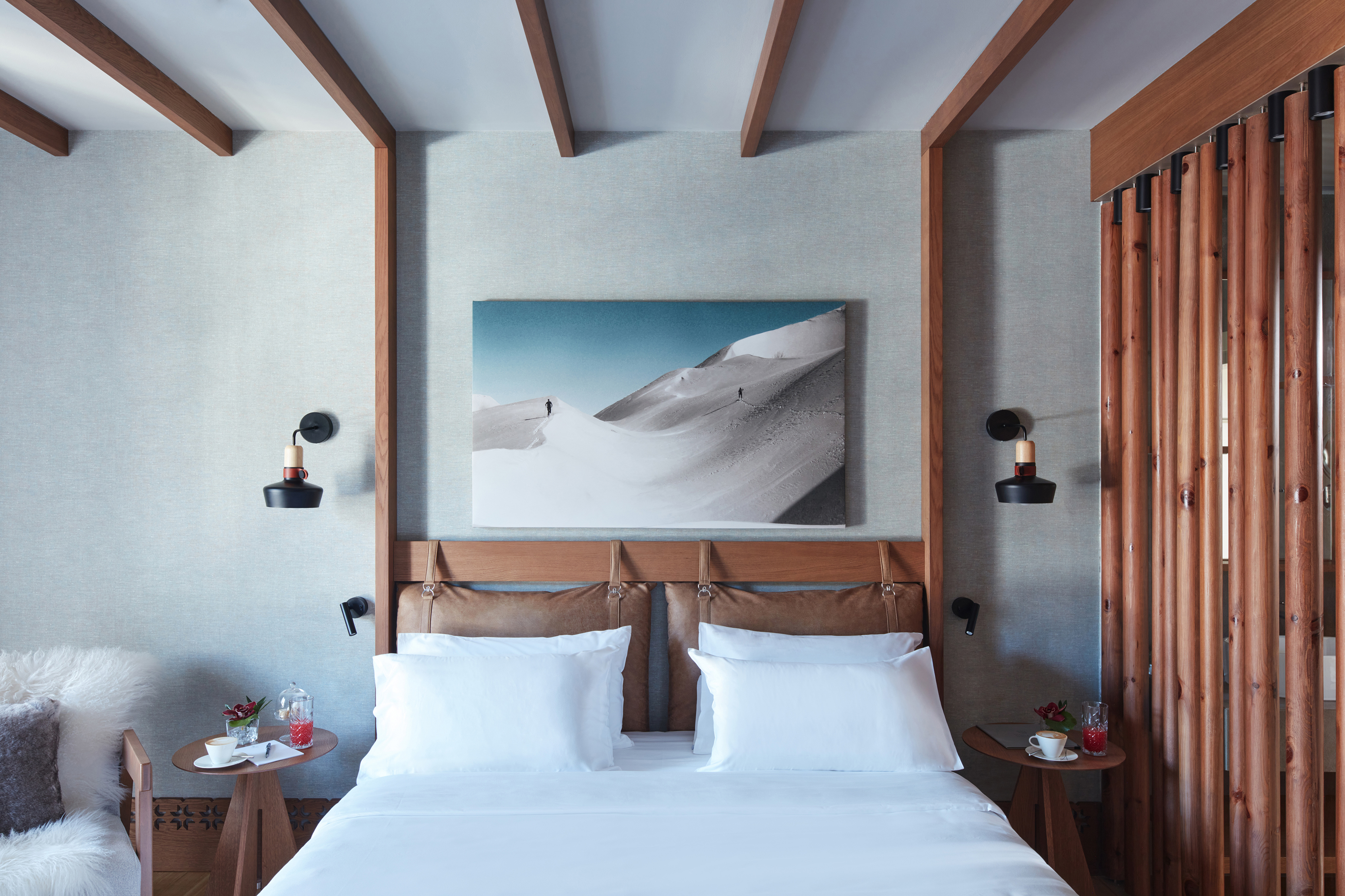 The bed area of a Superior Collection Room at Grand Hotel Savoia featuring a bed with skiing artwork overhead and flanked by tables beneath beamed ceilings