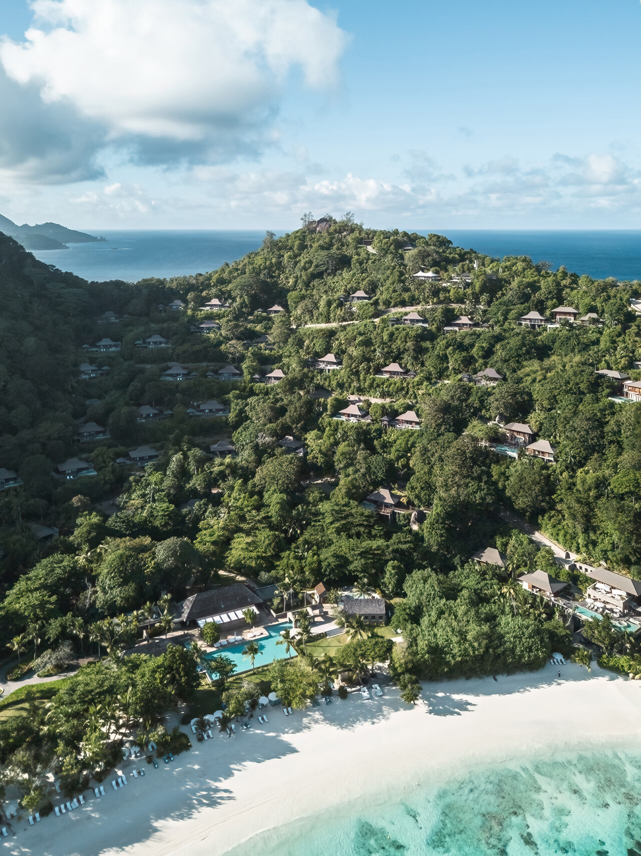Villas of Four Seasons Seychelles scattered over the hillside down to a white sandy beach 