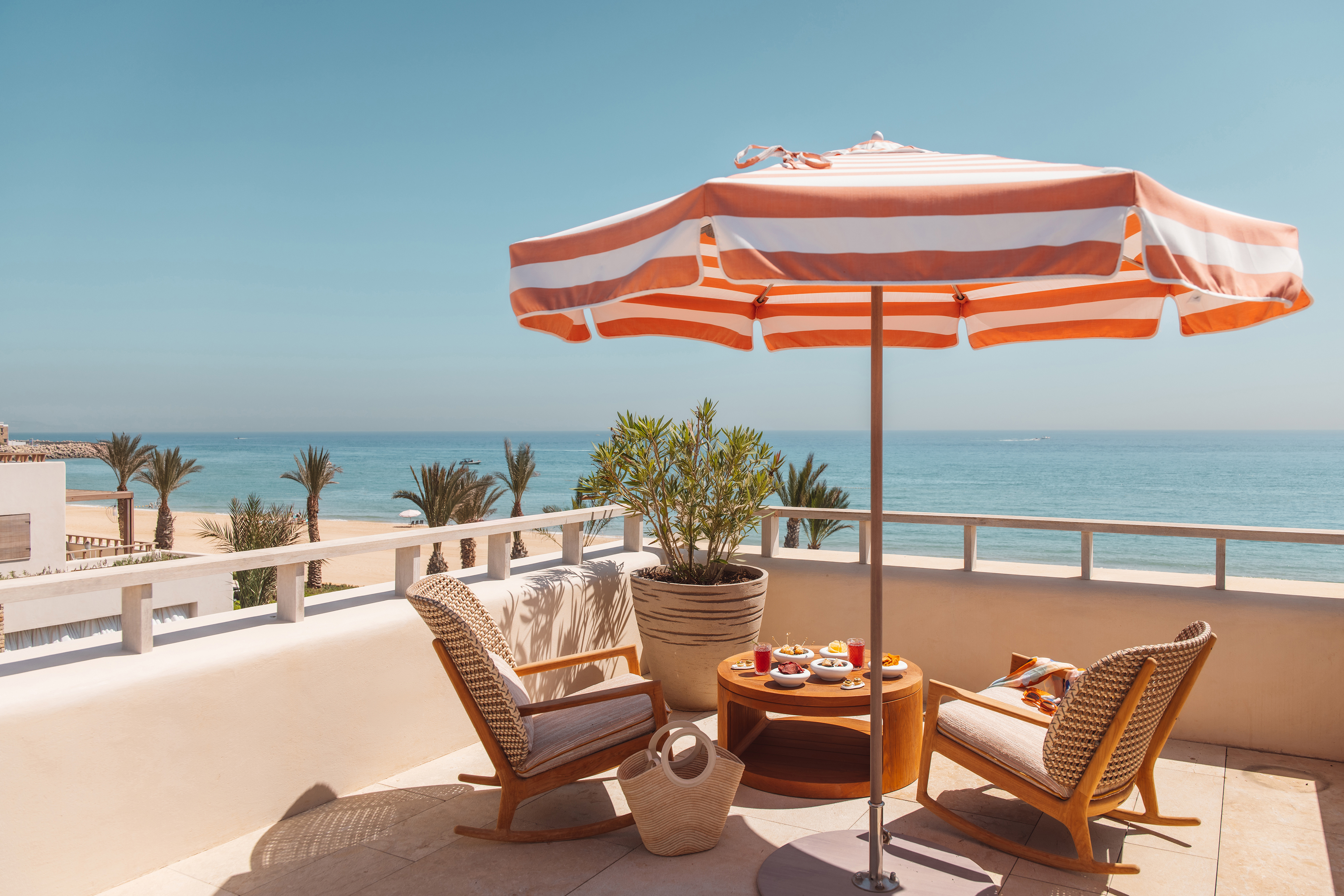 An outdoor terrace at Royal Mansour Tamuda Bay with lounge chairs beneath a striped umbrella looking out to the ocean