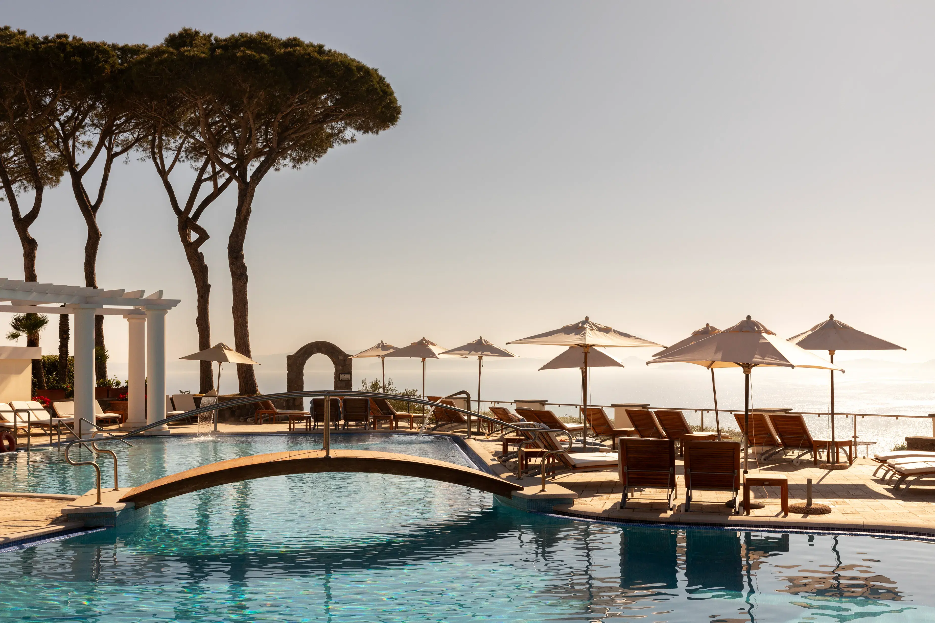 Luxurious pool area with sun loungers and umbrellas at San Montano Resort on Ischia, overlooking the sea with a serene sunset backdrop.