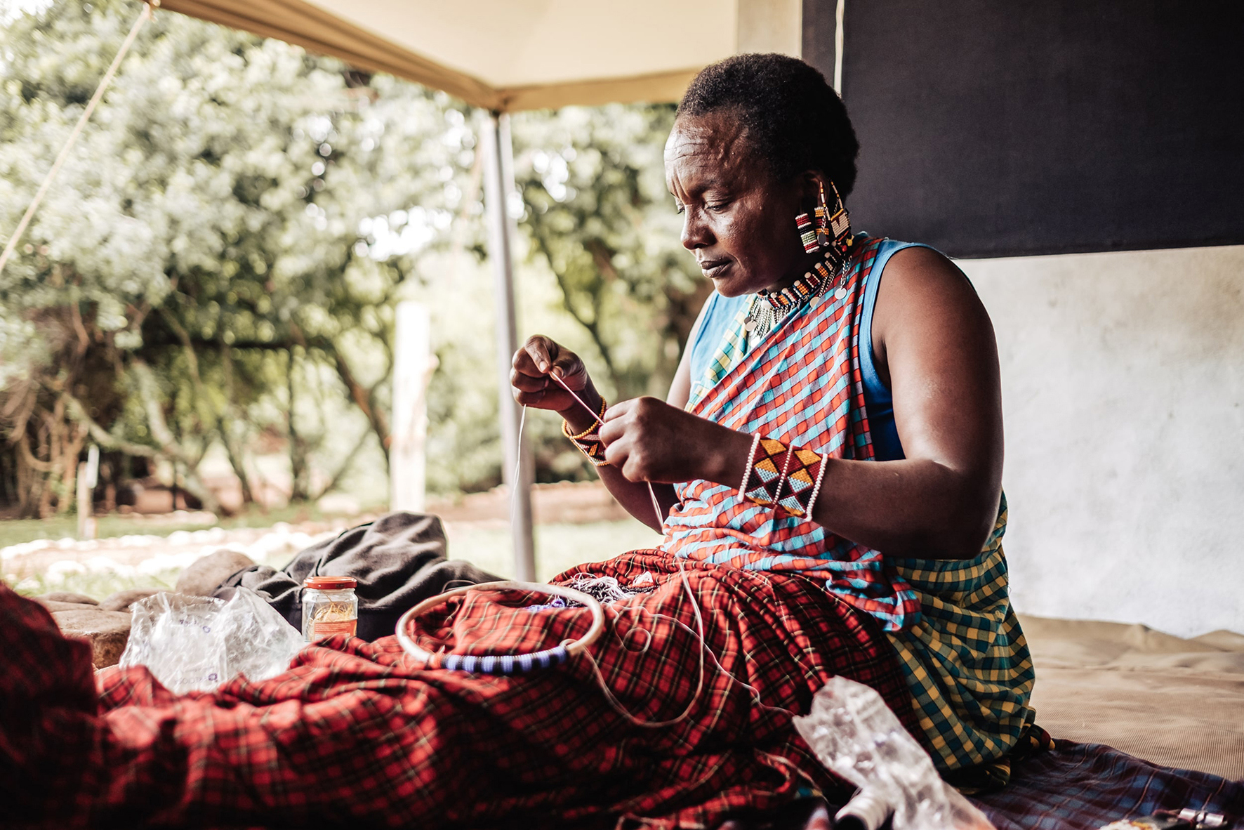 Maasai woman in traditional dress threading beads onto a piece of jewellery 