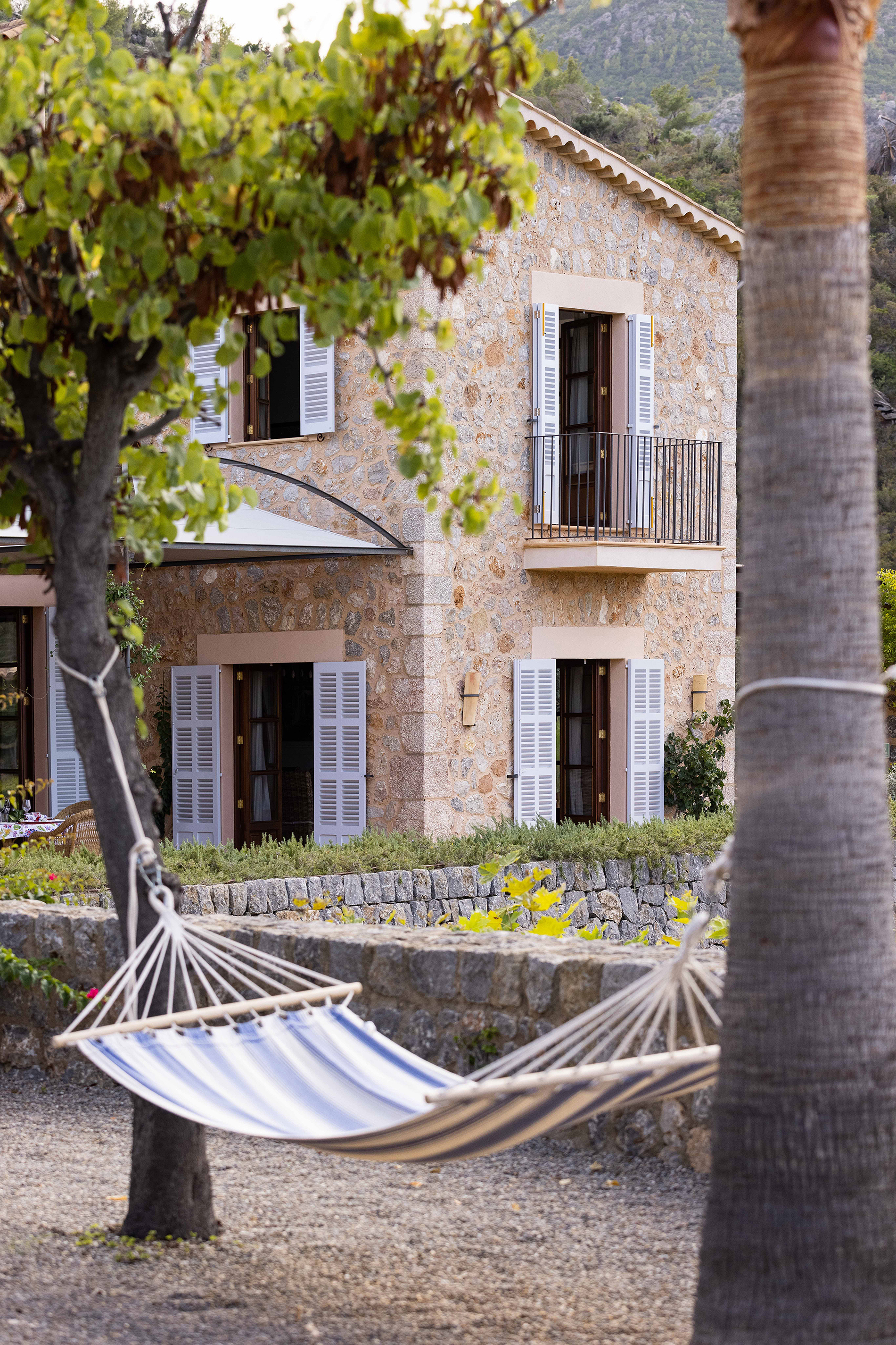 Blue and white striped hammock between two trees in front of stone building