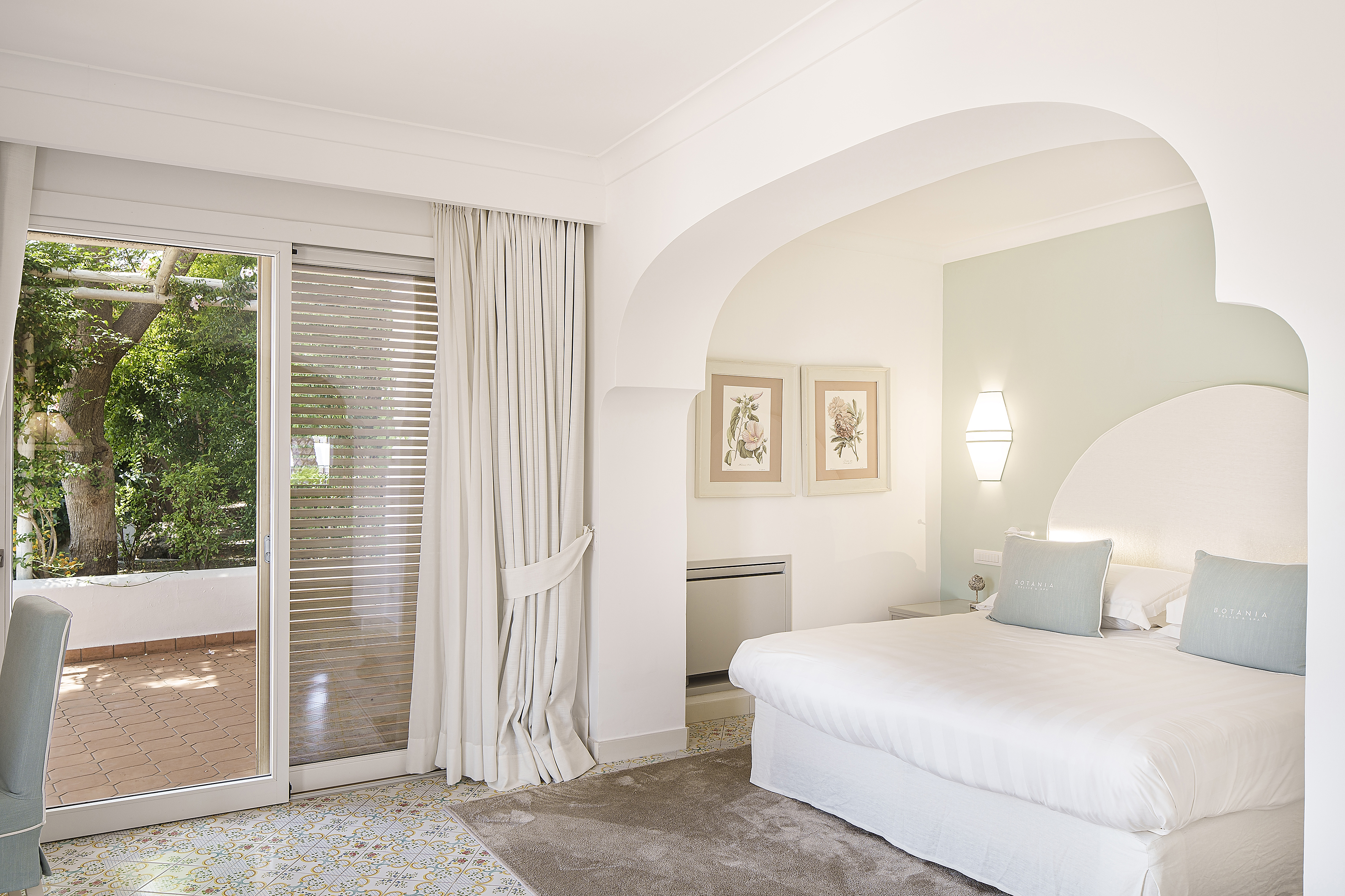 Luxurious room at Botania Relais & Spa in Ischia featuring a king-sized bed, elegant decor, and a view of the lush garden through large sliding glass doors.