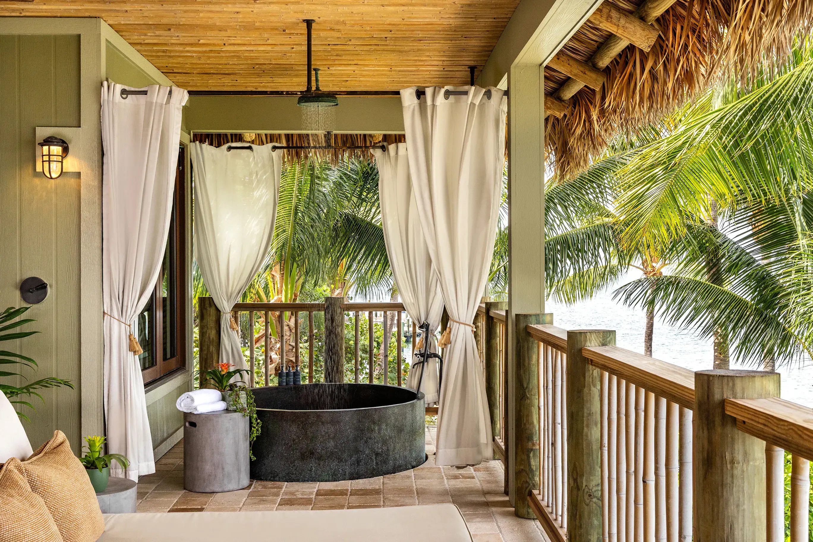 Private outdoor soaking tub on a thatched-roof terrace of a Premier Suite overlooking palm trees and ocean at Little Palm Island Resort in Florida.