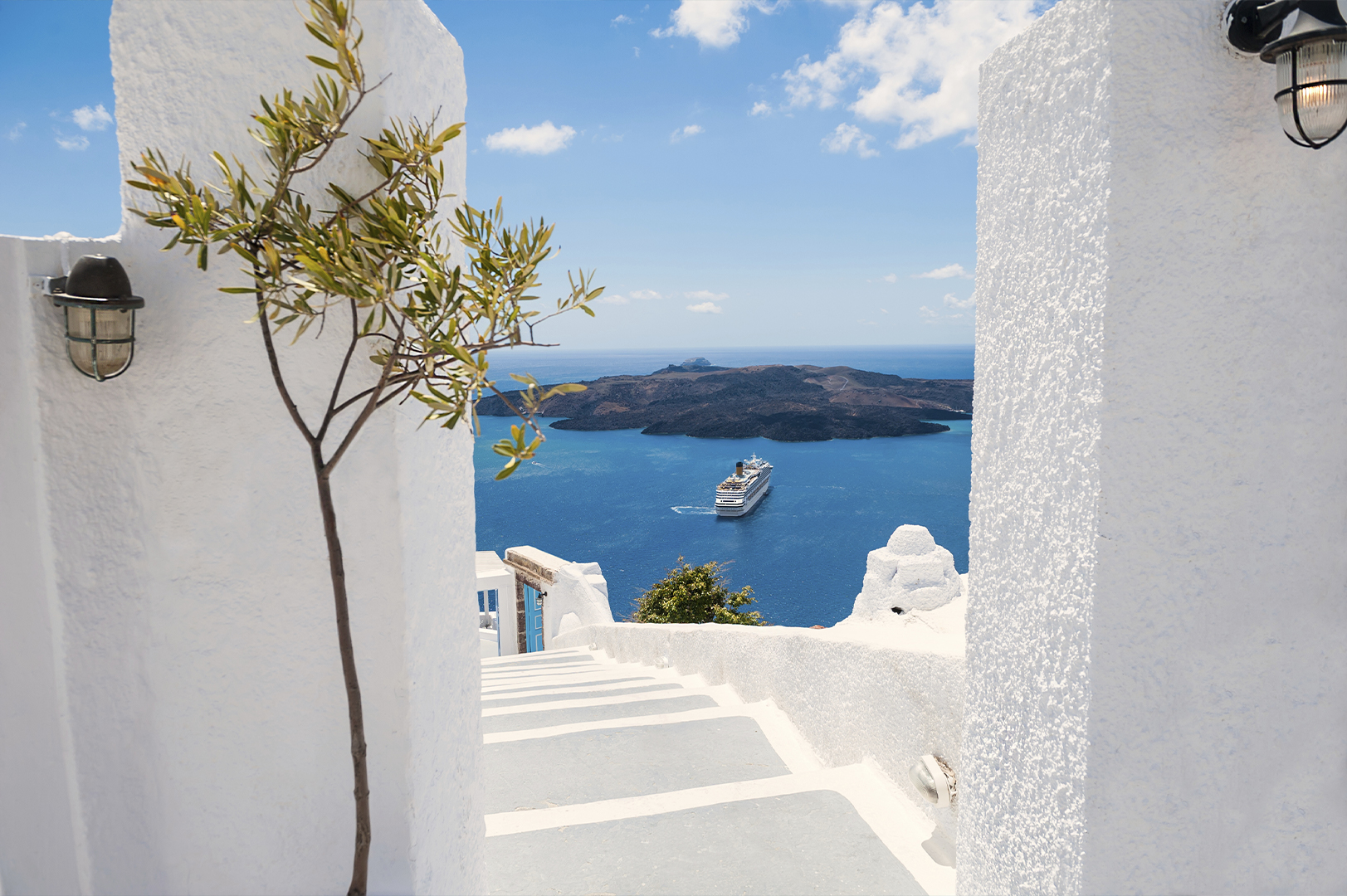A view through a white archway with steps leading down towards the sea, featuring a cruise ship in the distance and clear blue skies.