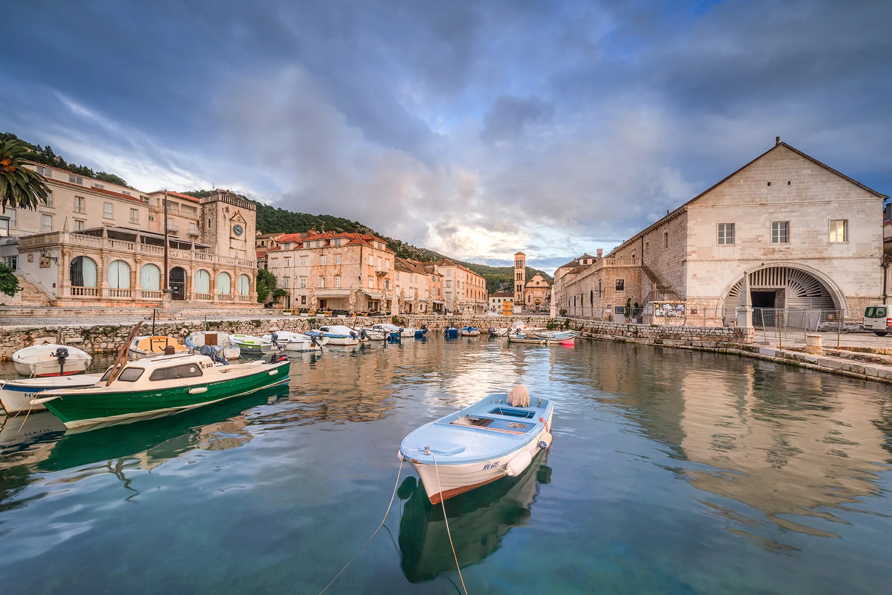 Small boats floating in Hvar Town’s historic harbor, surrounded by stone buildings and a waterfront under dramatic clouds.