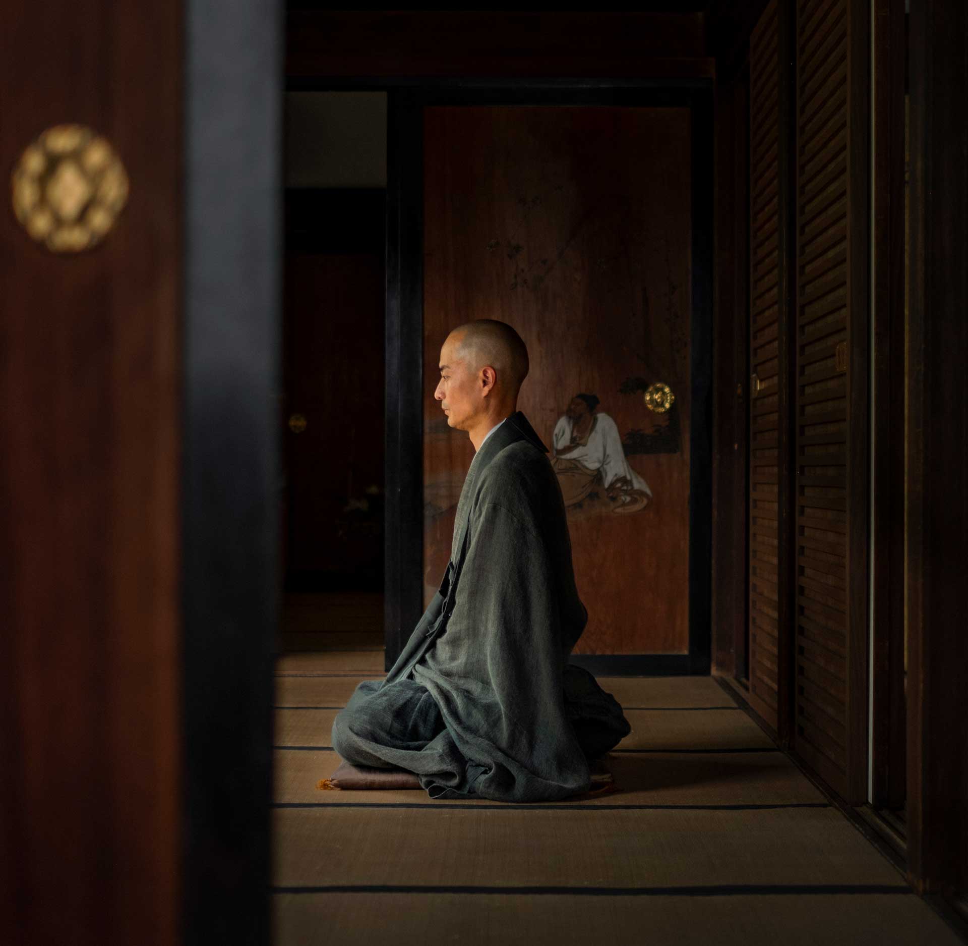 Person seated in quiet meditation inside a traditional wooden room with sliding panels and soft natural light.