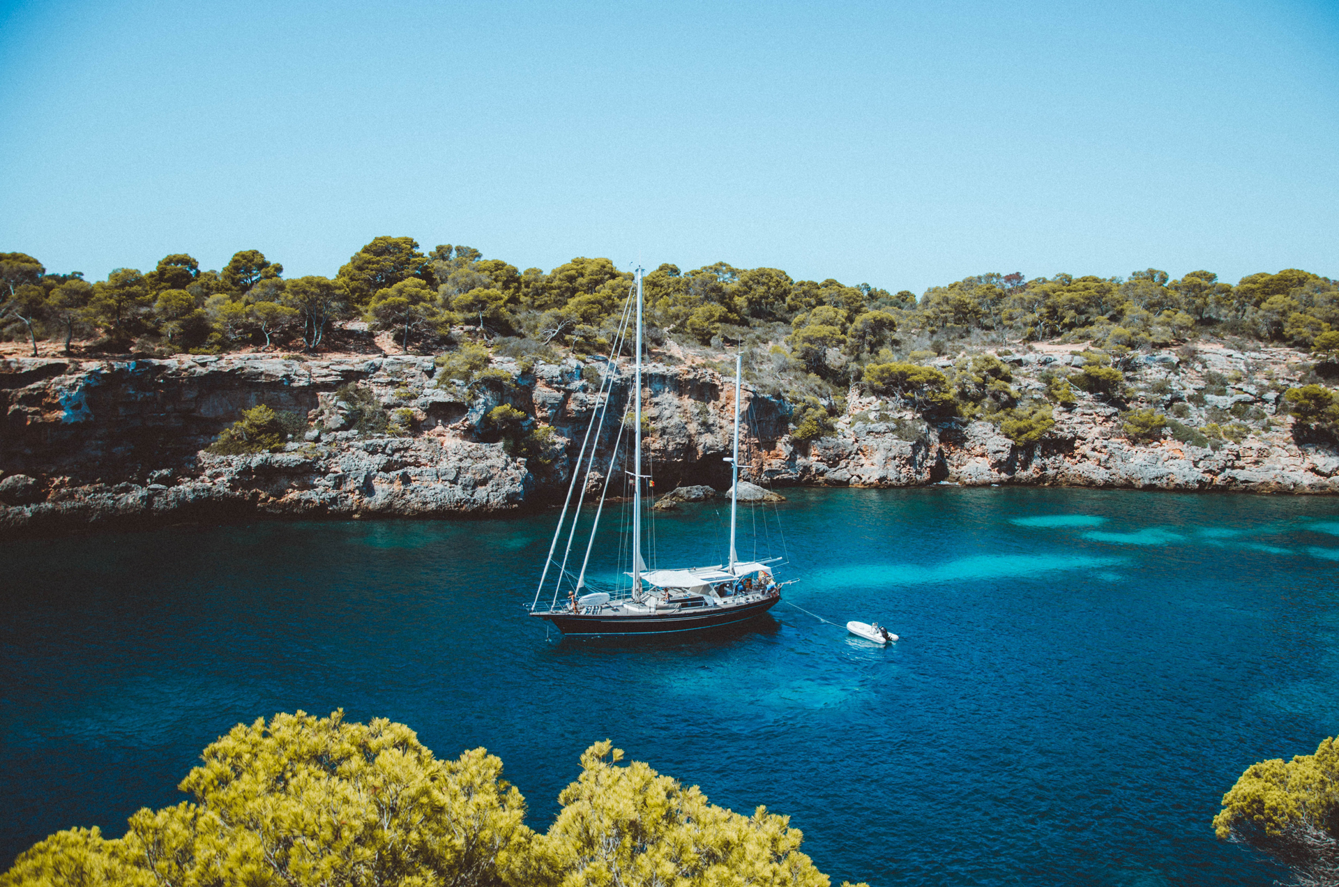 Brown and white sailboat in between rocky coastlines