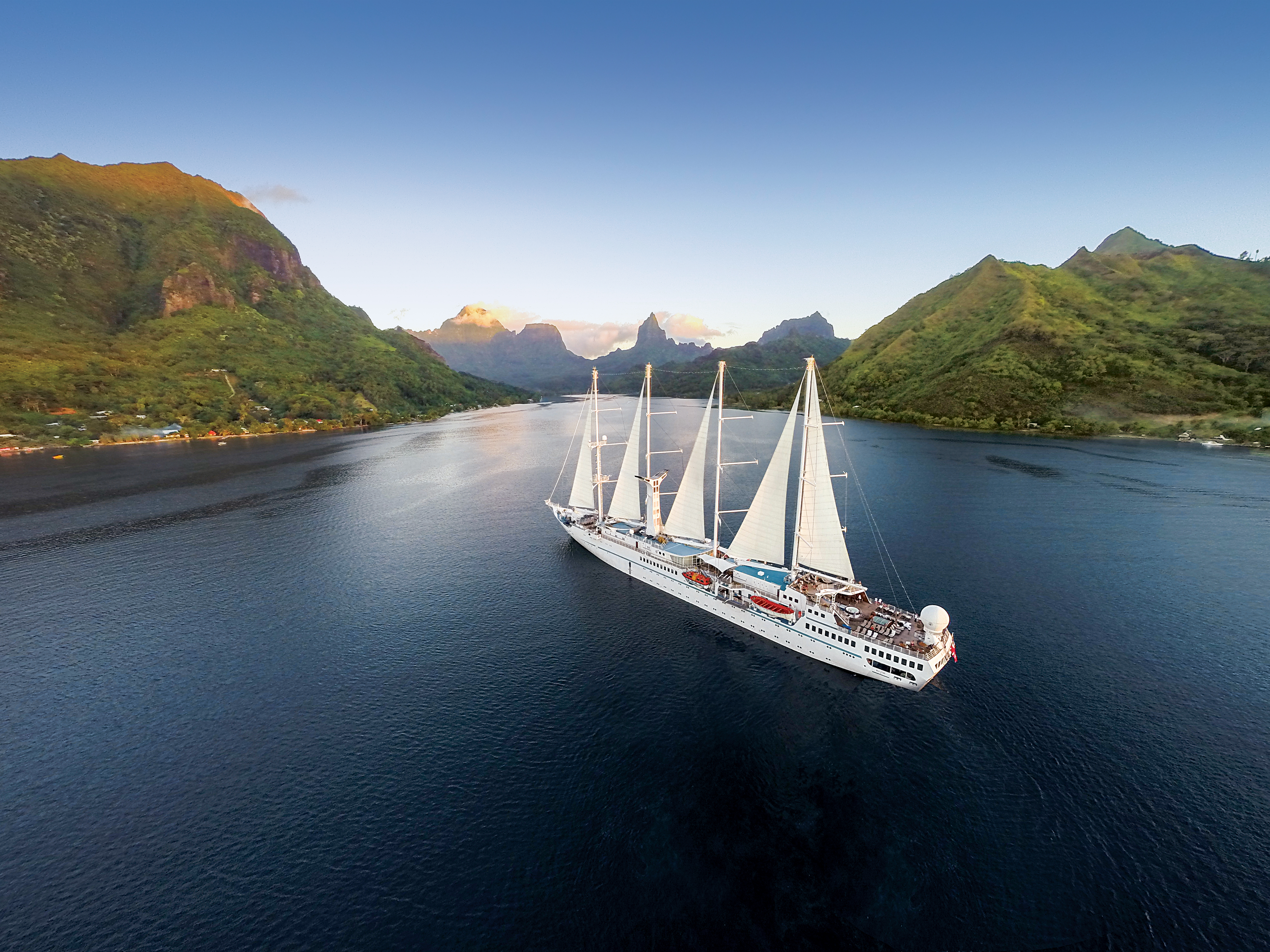 The large masted sailing yacht Wind Spirit of the Windstar fleet in a wide bay backed by lush green mountains