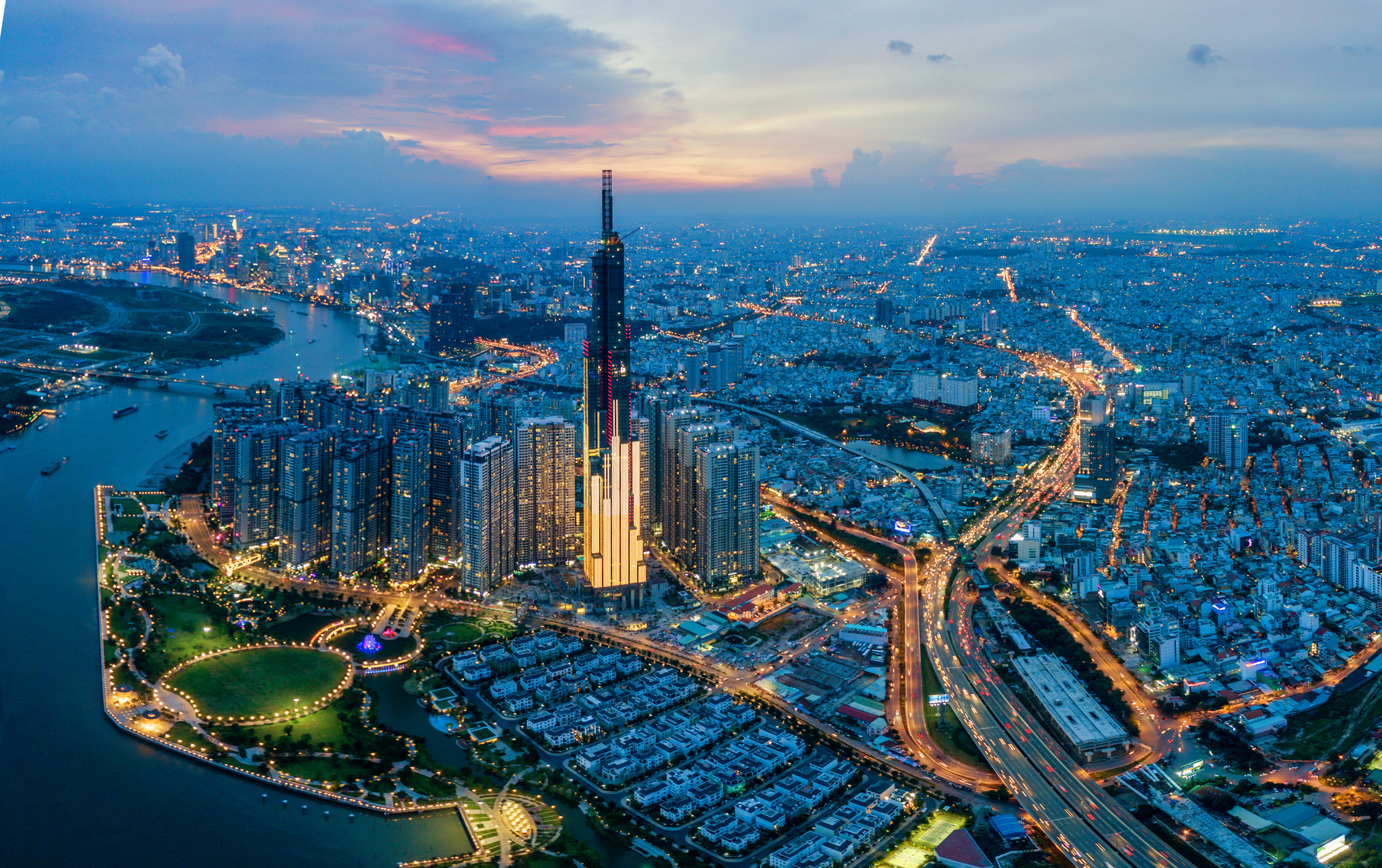 Aerial view of a cityscape at dusk with illuminated skyscrapers and busy traffic.