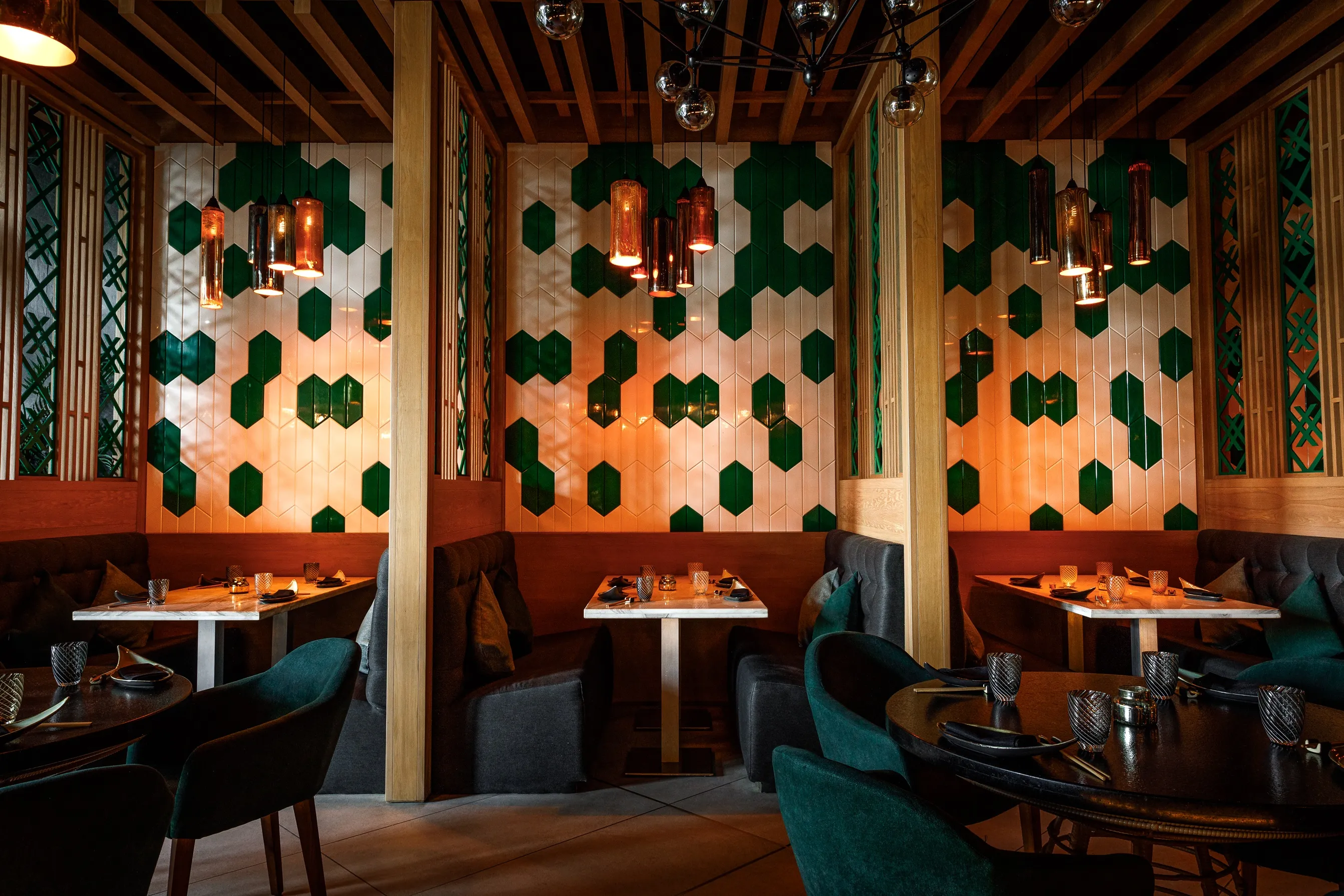 Warm, modern restaurant interior with green geometric wall tiles, wooden accents and softly lit pendant lights.