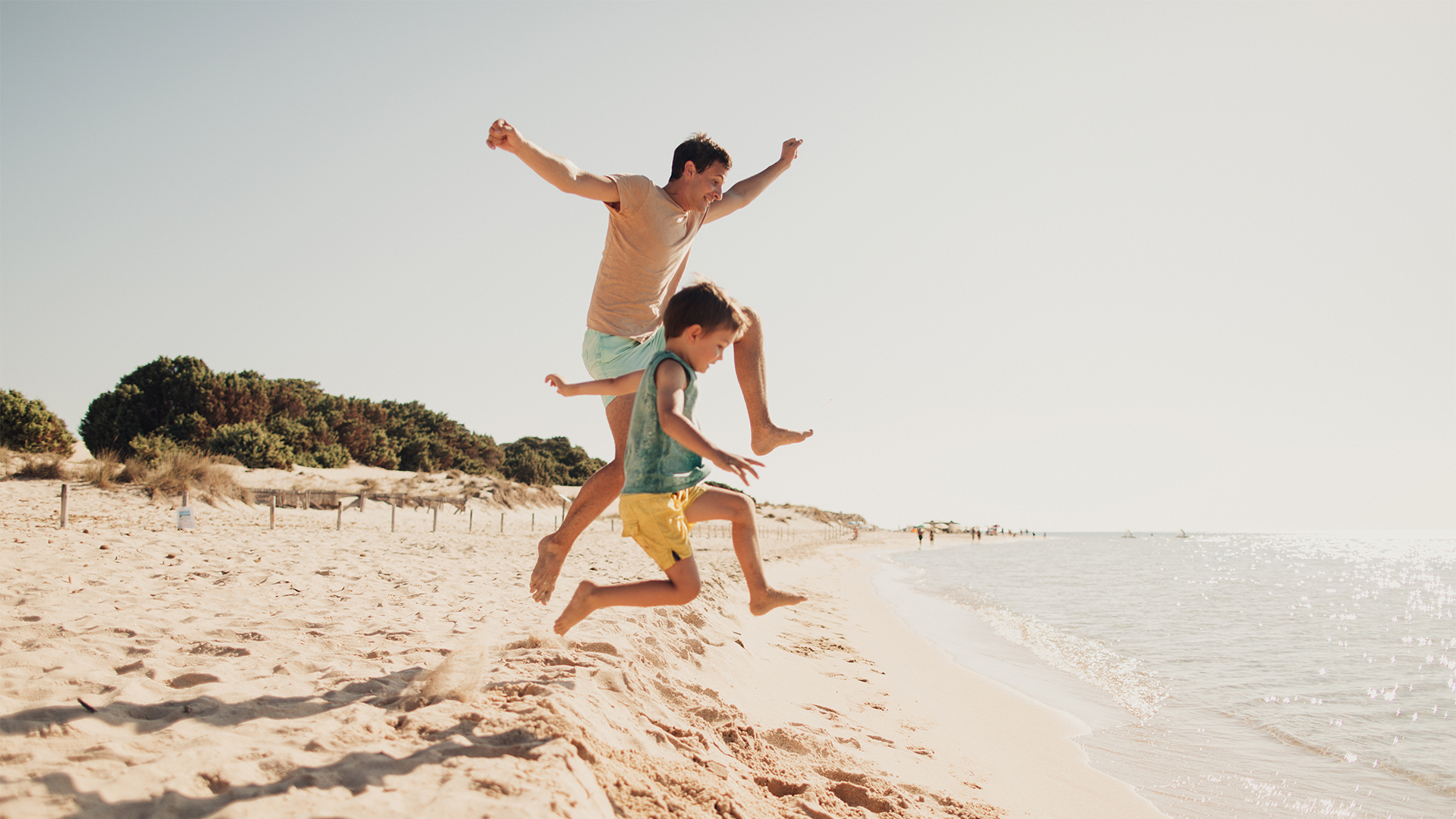 Father and son running down the beach to the sea