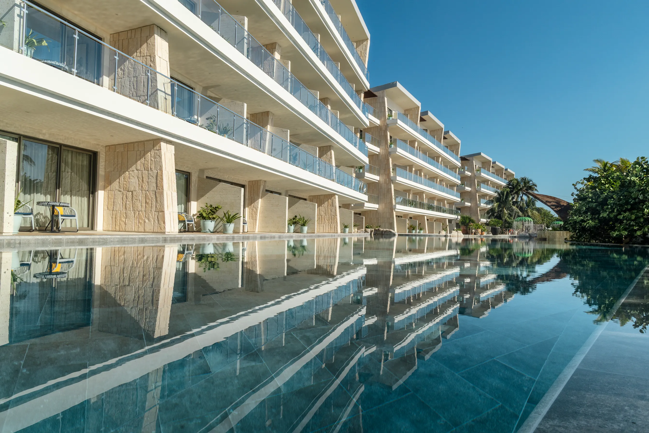 Modern beachfront hotel with swim‑up rooms reflected in a long pool.