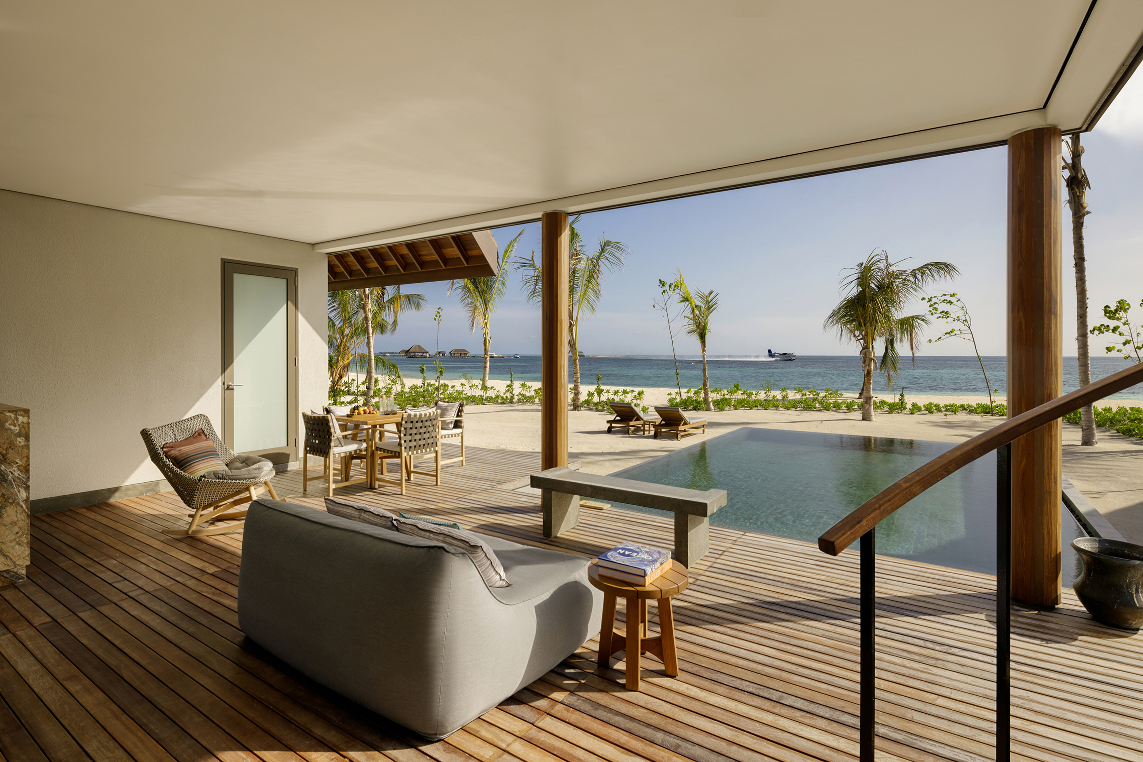 Decking with sofa and coffee table looking out over the pool and beach with sea plane landing in a beach retreat at Six Senses Kanuhura