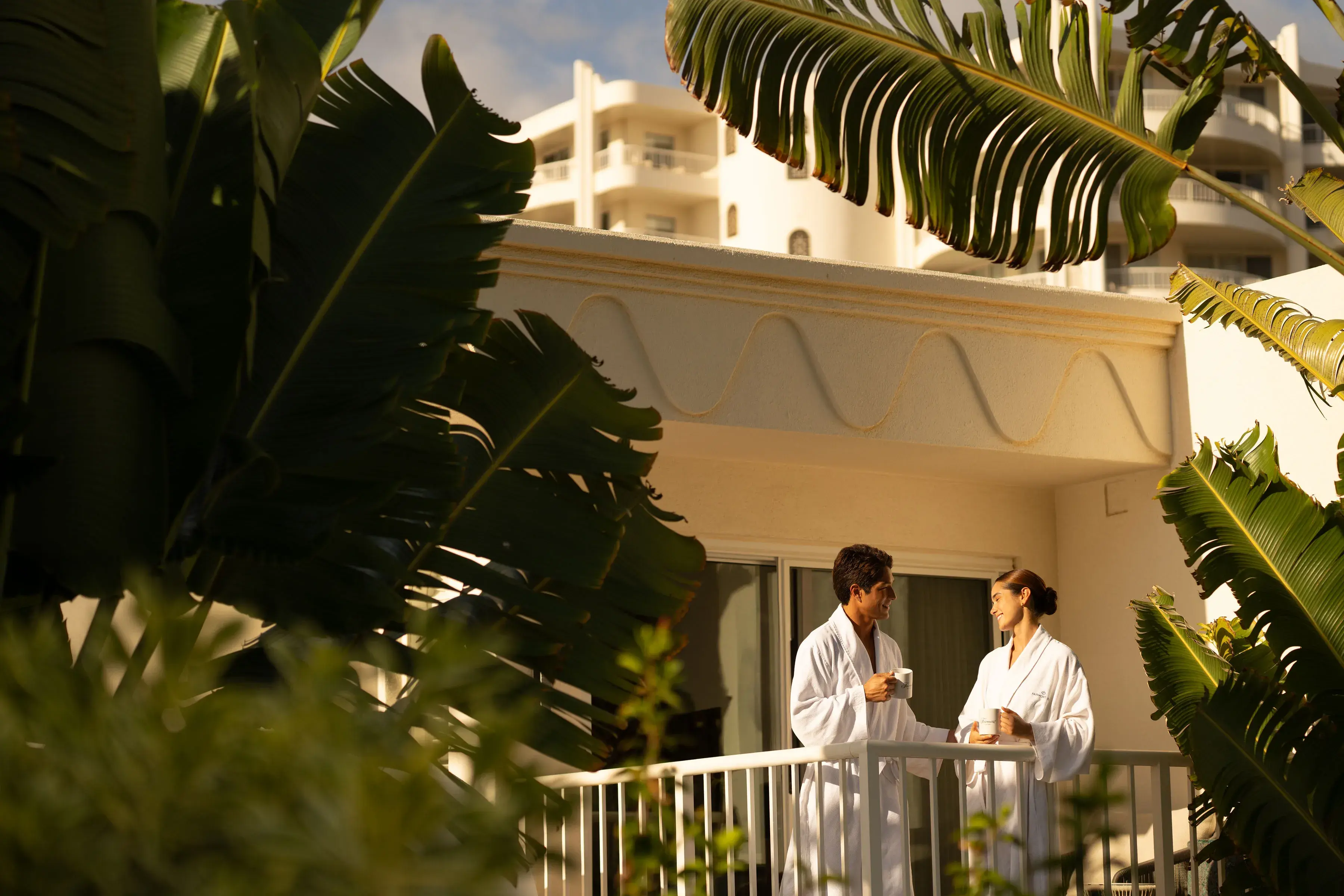A couple in dressing gowns having a drink on the terrace of the spa at Fairmont Kea Lani surrounded by lush palm leaves