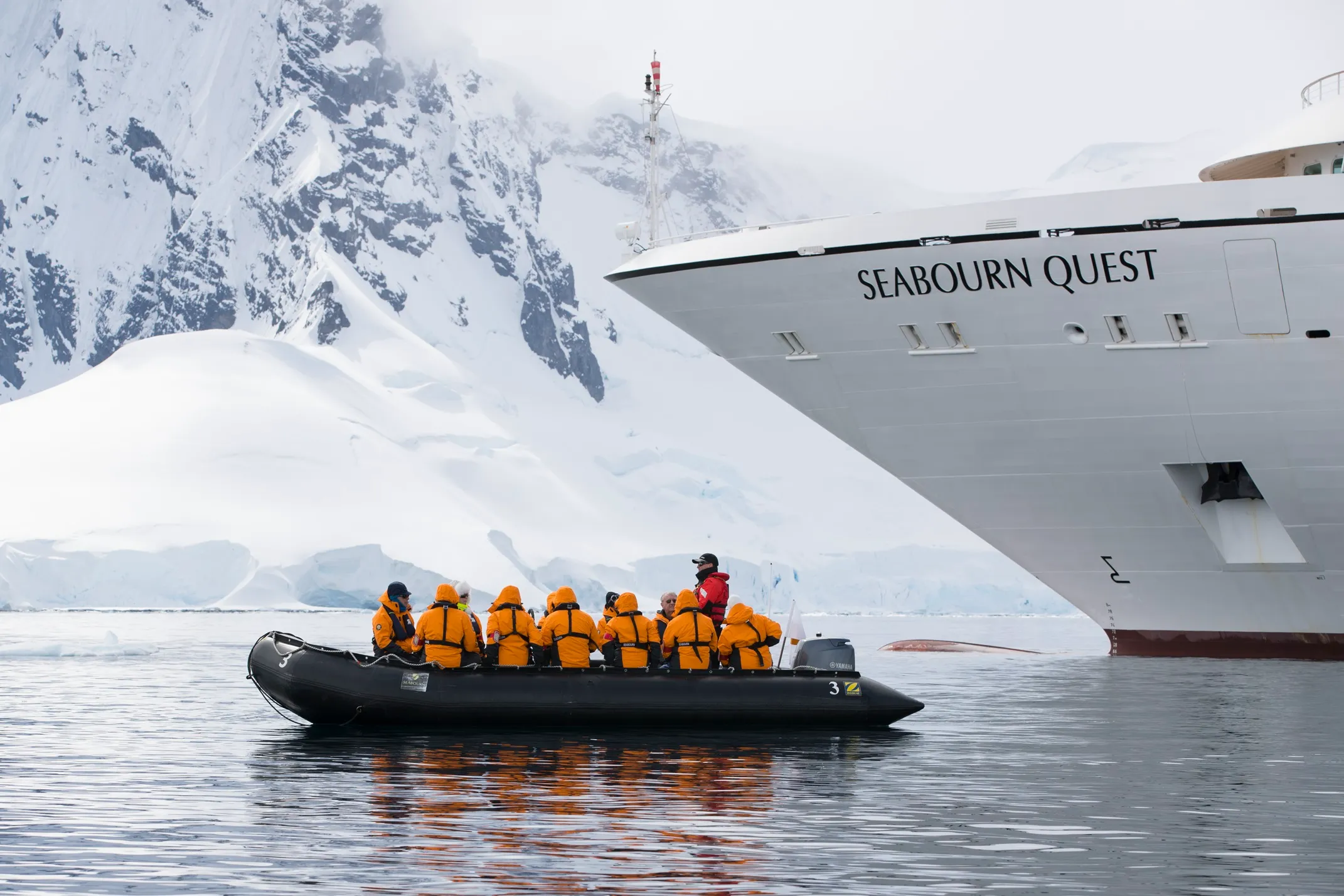 Group in orange jackets on a small Zodiac boat near Seabourn Quest cruise ship with snowy mountains in the background.