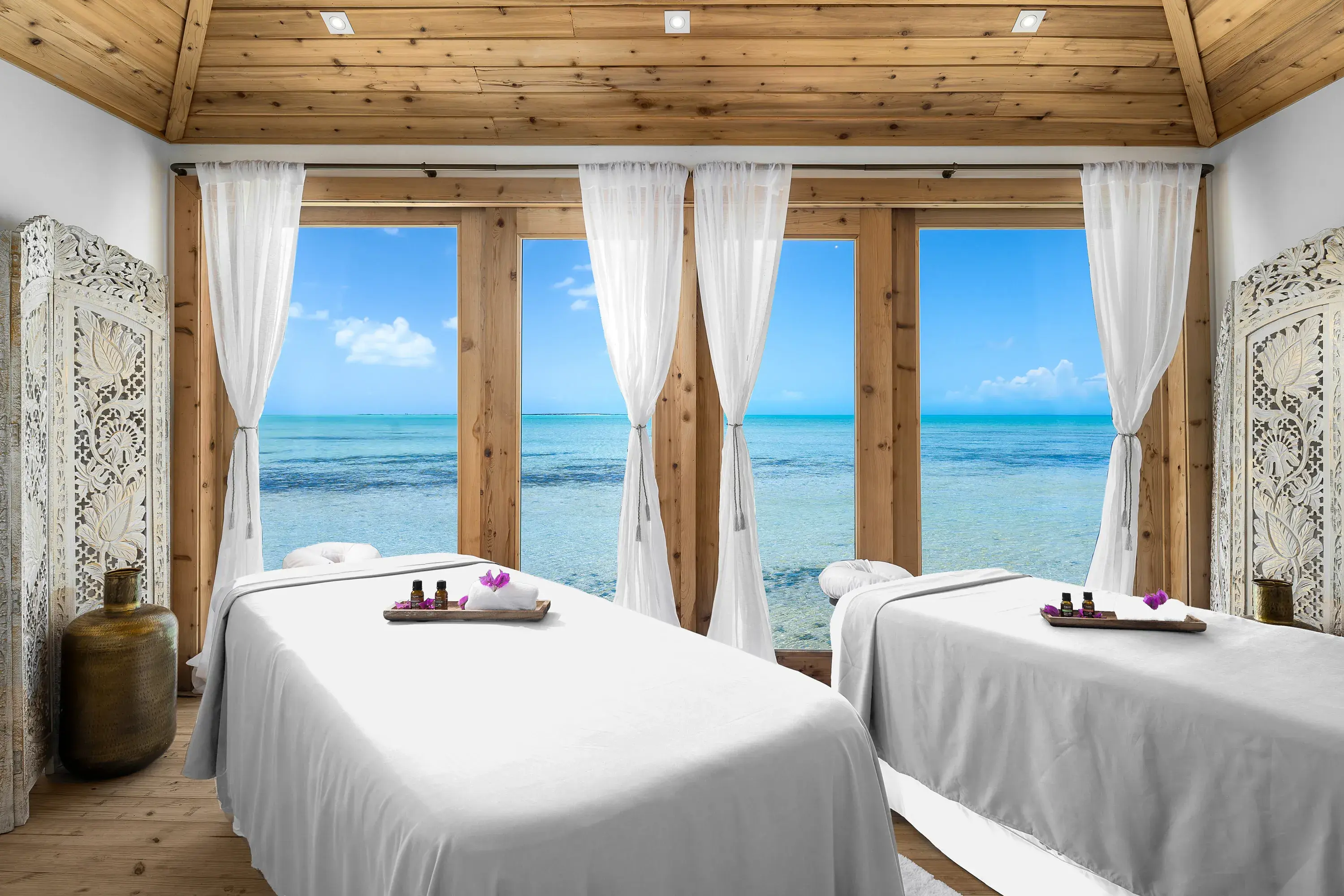 A relaxing spa room at Ambergris Cay in Turks & Caicos featuring two massage tables in a wooden room with large windows looking out over the sea