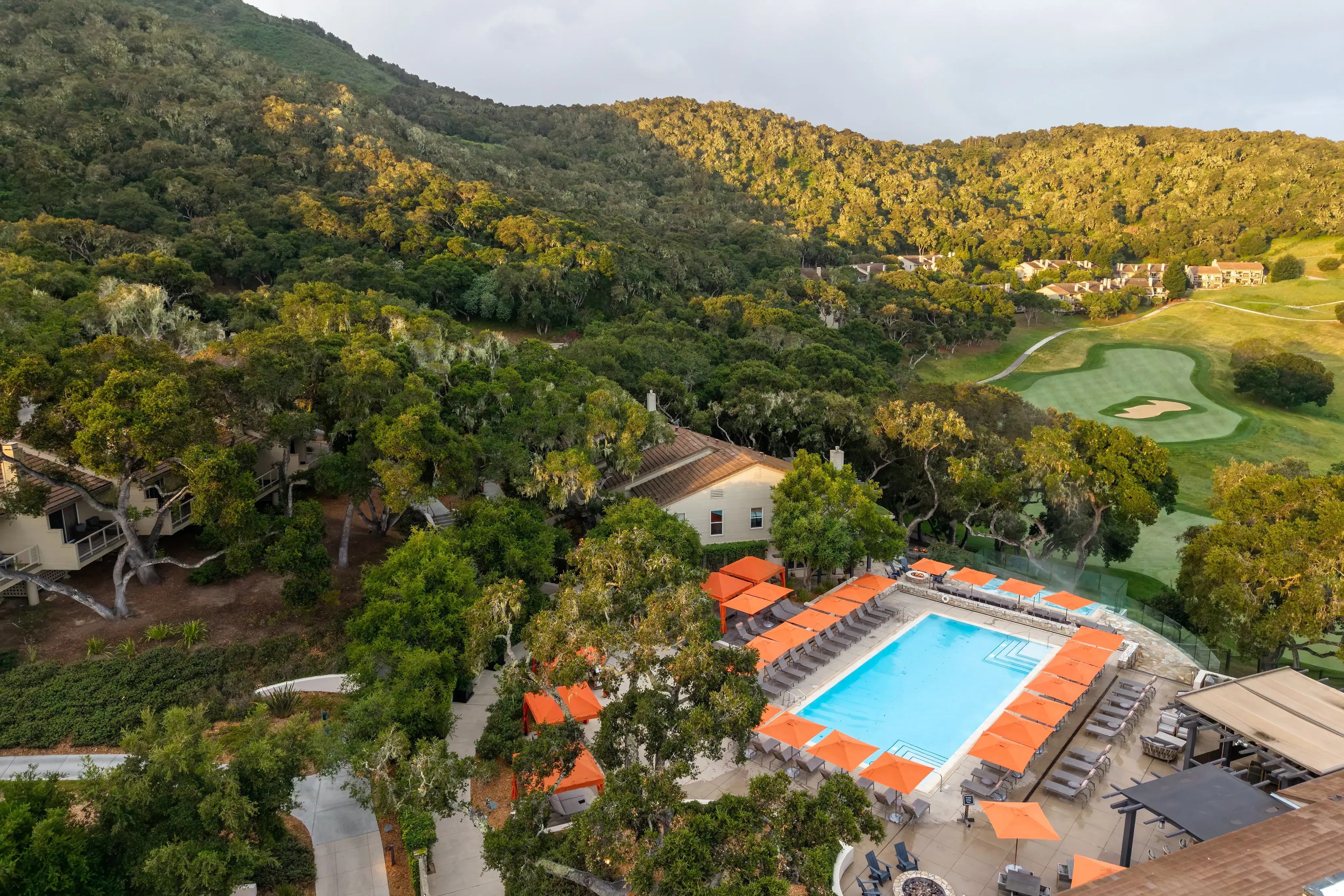 The lodge and swimming pool at Carmel Valley Ranch in California set among greenery on the side of a hill with a glimpse of a golf course behind