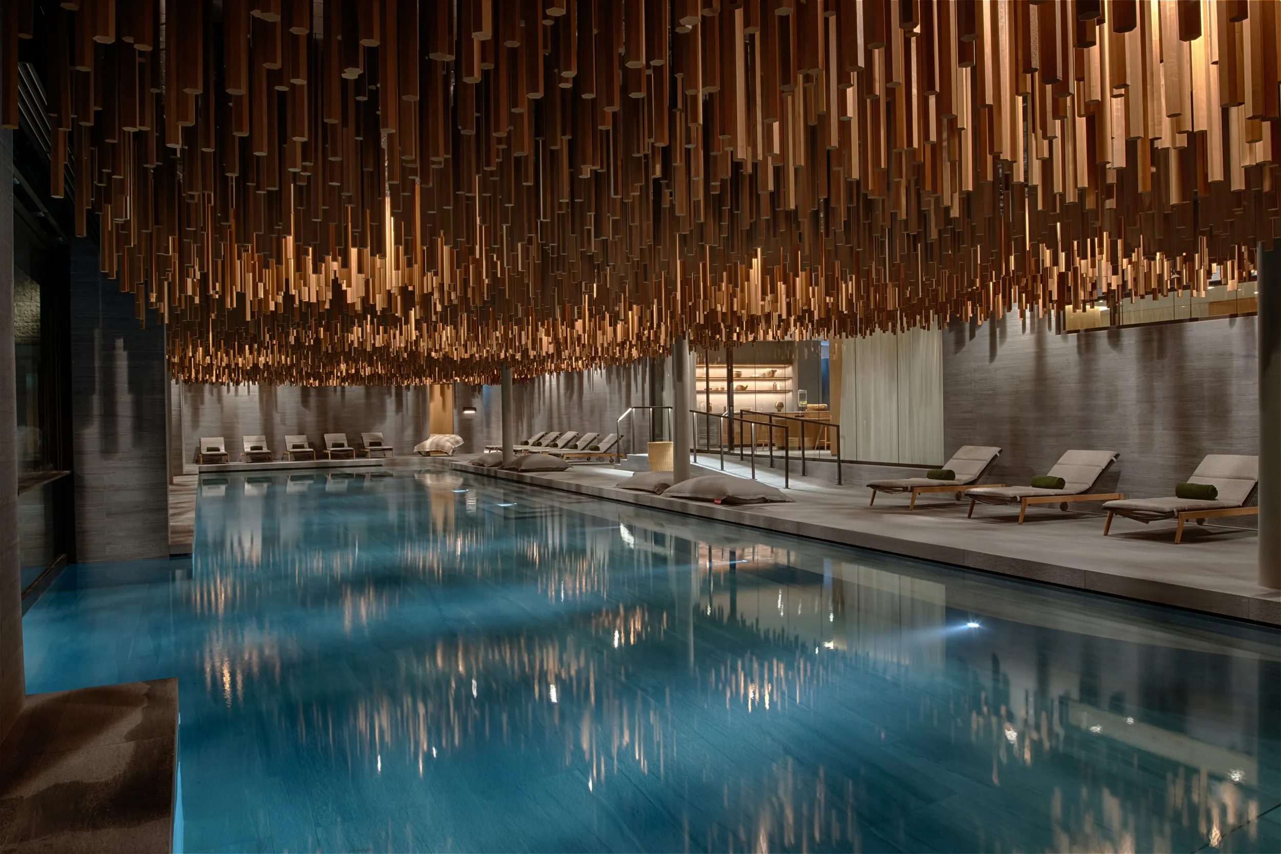 Elegant indoor swimming pool with lounge beds and sculptural ceiling installation.