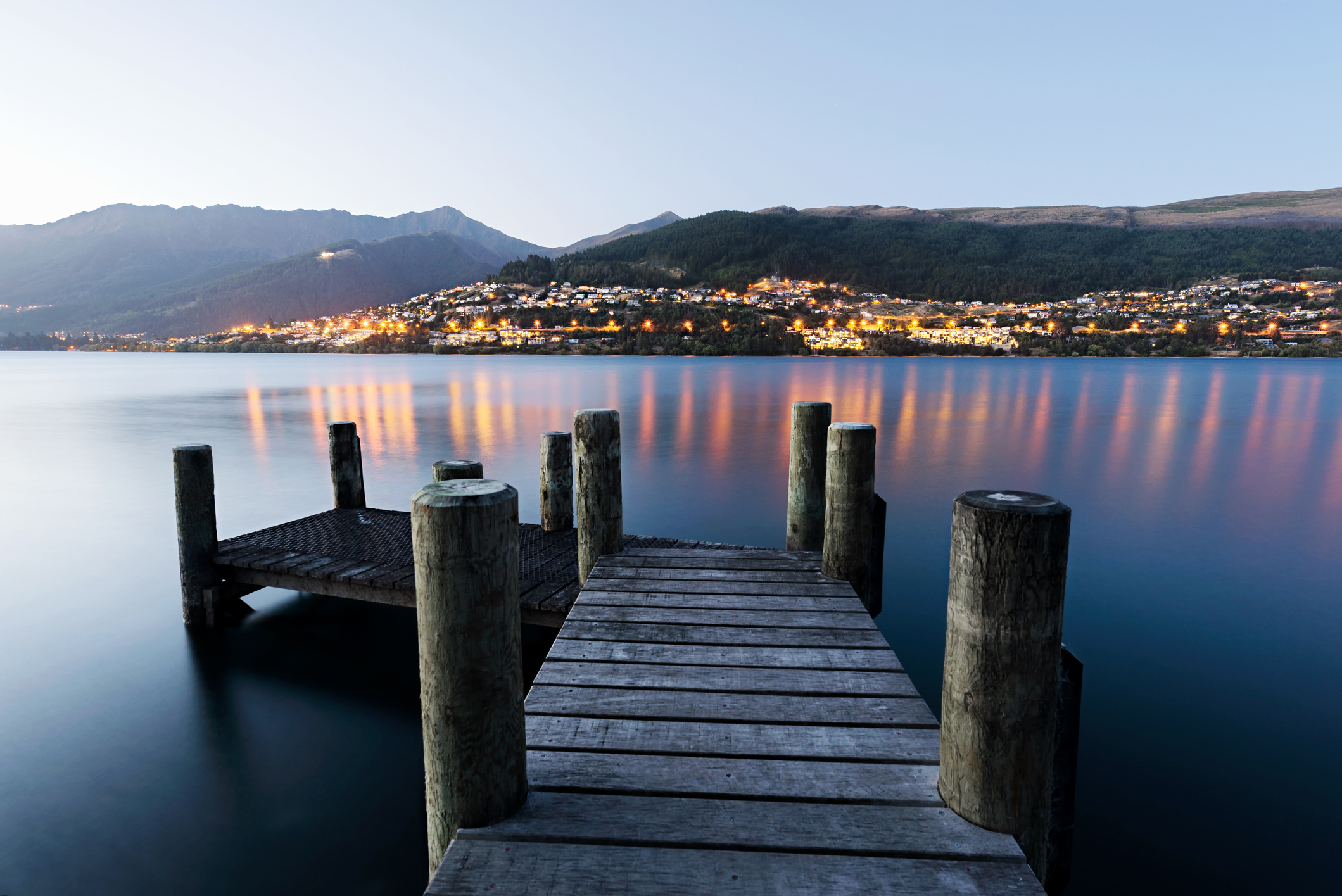 Wooden pier looking across the bay to Queenstown lit up in the evening