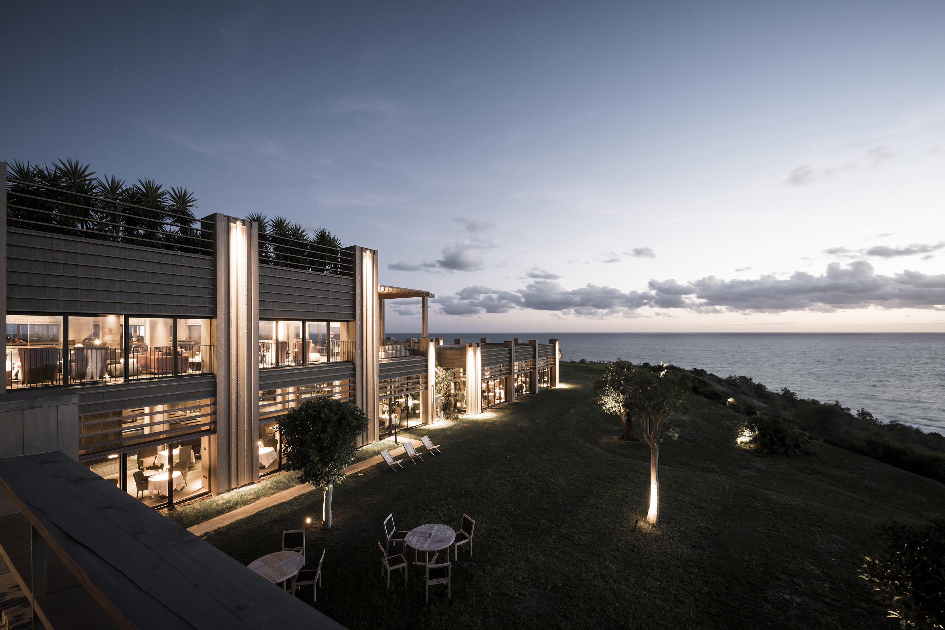 Exterior of hotel lit up at sunset with lights illuminating greenery on the lawn