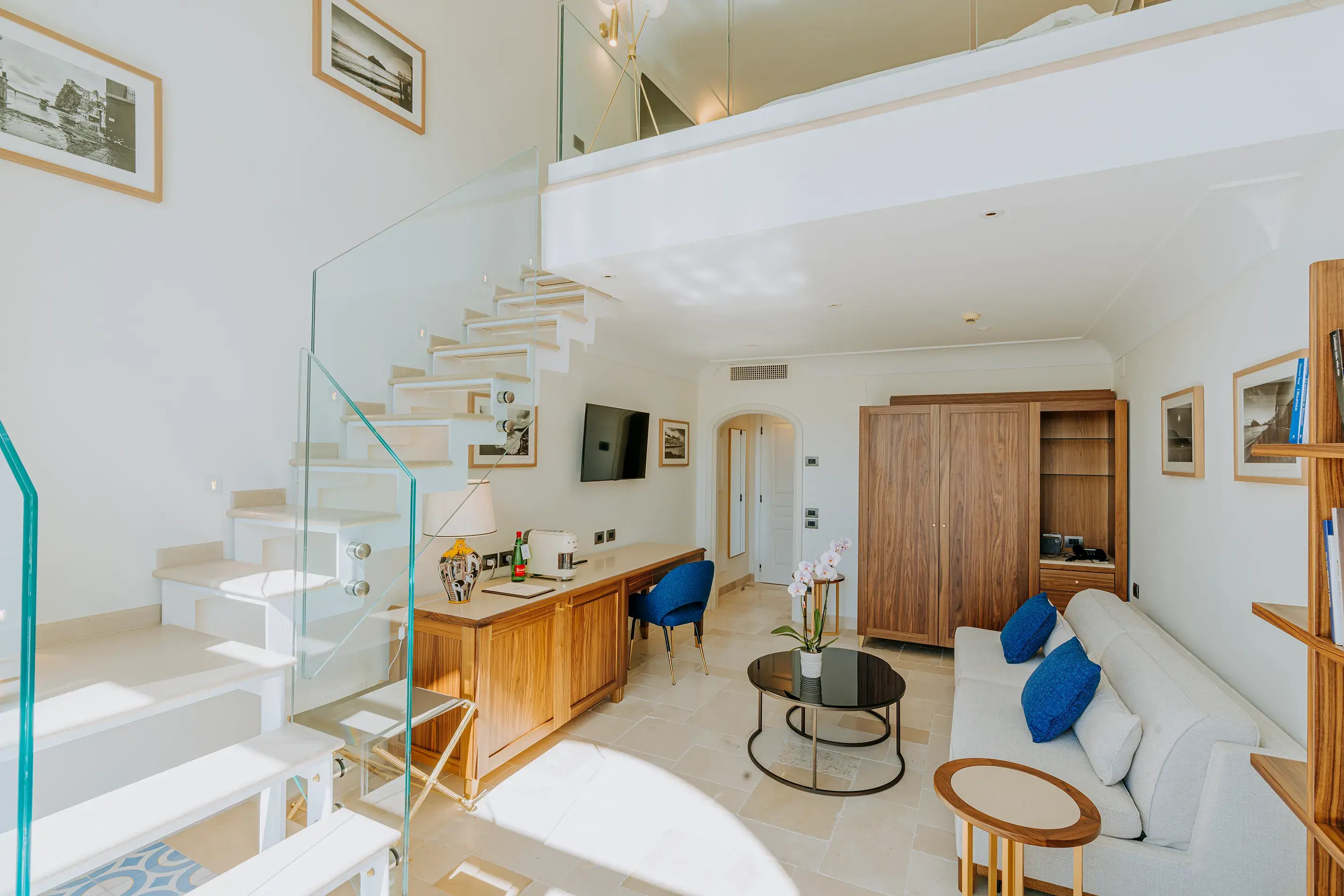 Luxurious duplex suite at San Montano Resort on Ischia featuring modern decor, a glass staircase, and spacious living area with wooden furnishings.