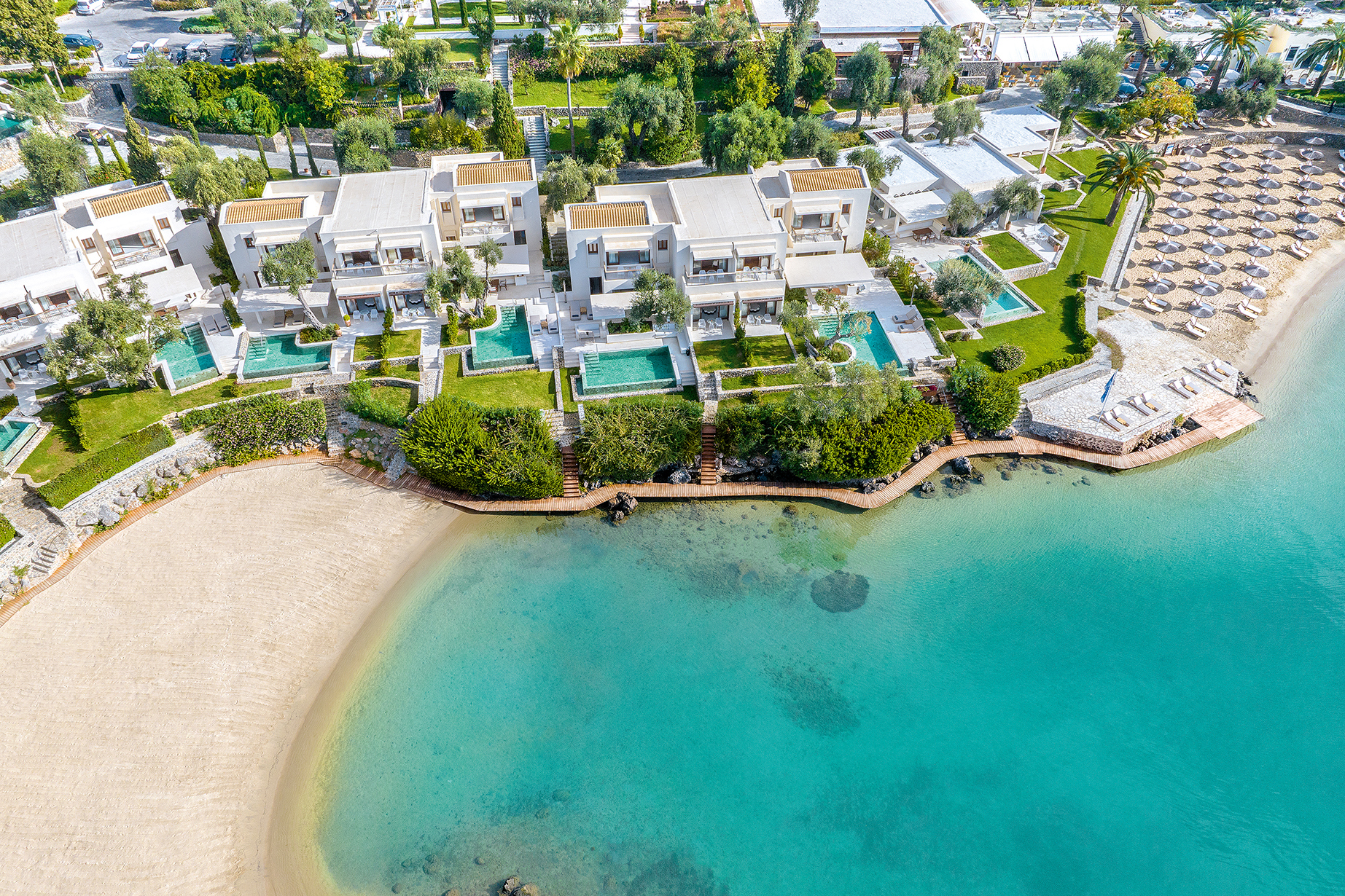 Aerial view of beachfront villas with private pools at Grecotel Corfu Imperial, set amid lush greenery and turquoise waters.